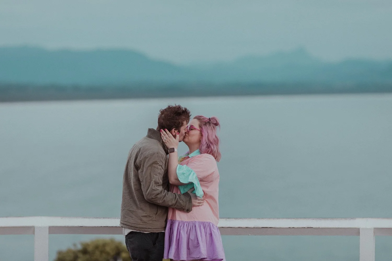 Newly engaged couple kissing at the lighthouse lookout with Byron Bay behind