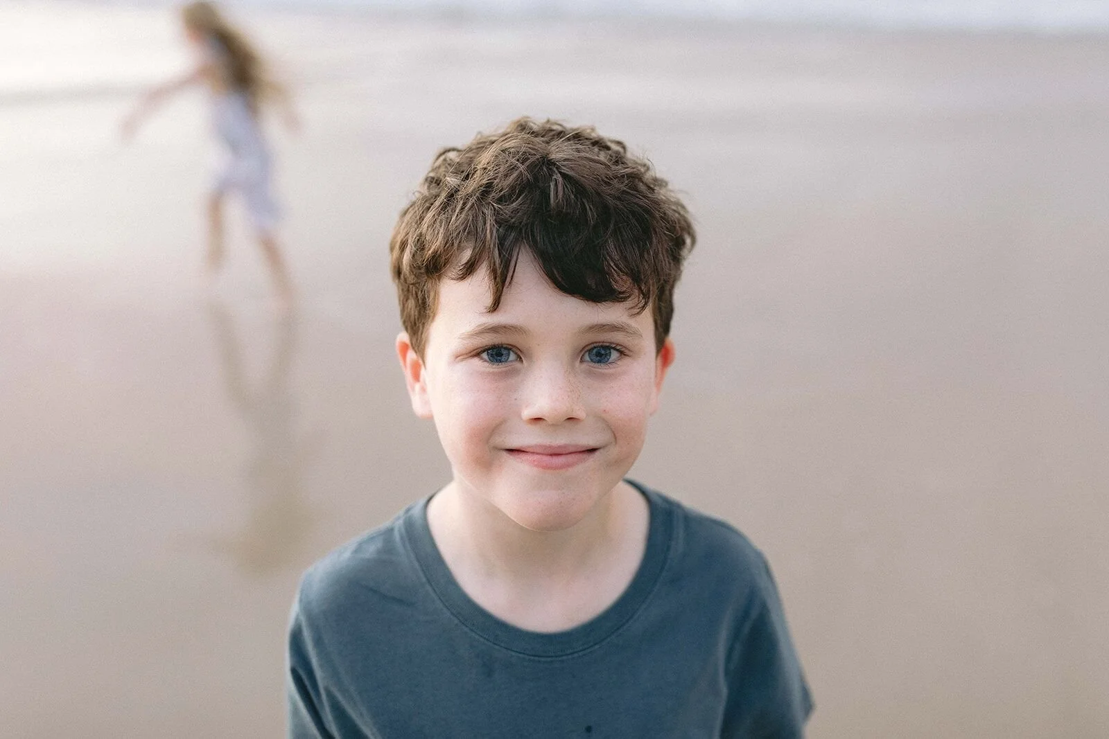 Portrait of a boy in a teal t-shirt smiling at the camera on the beach