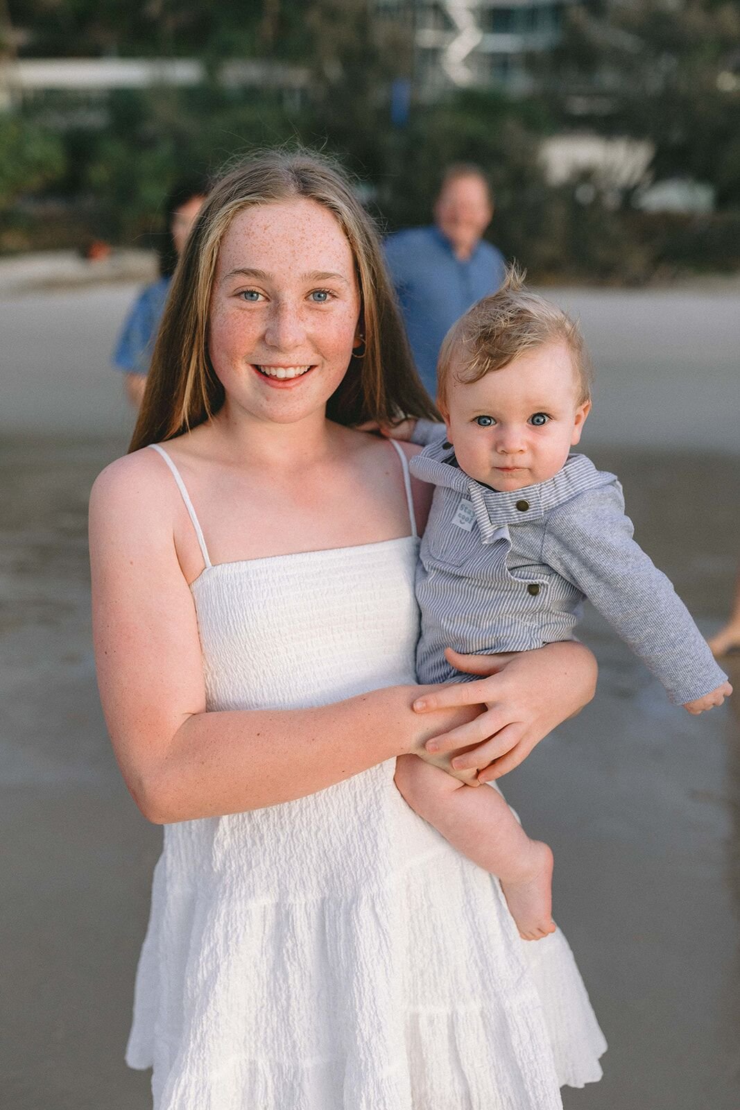 Smiling girl in a white dress holding her baby cousin in a grey jacket