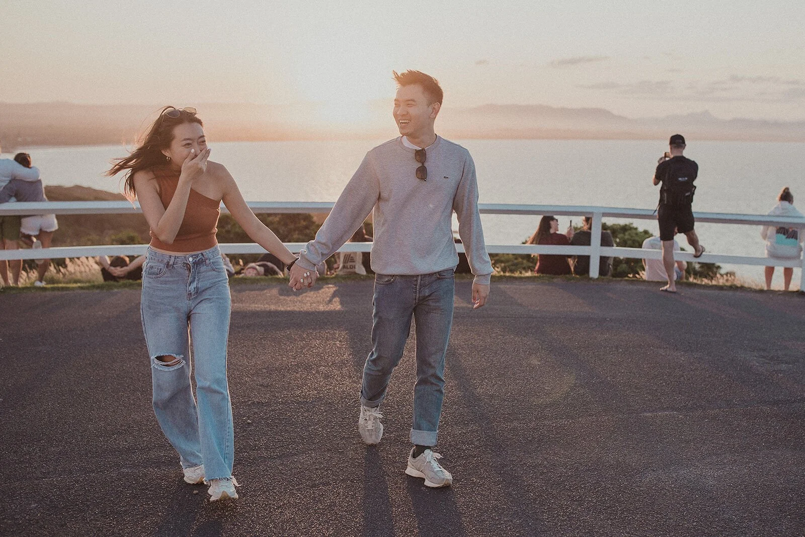 Couple walking hand in hand at the lookout, the woman laughing, Douglas and Ying's sunset marriage proposal at Cape Byron Lighthouse, Byron Bay