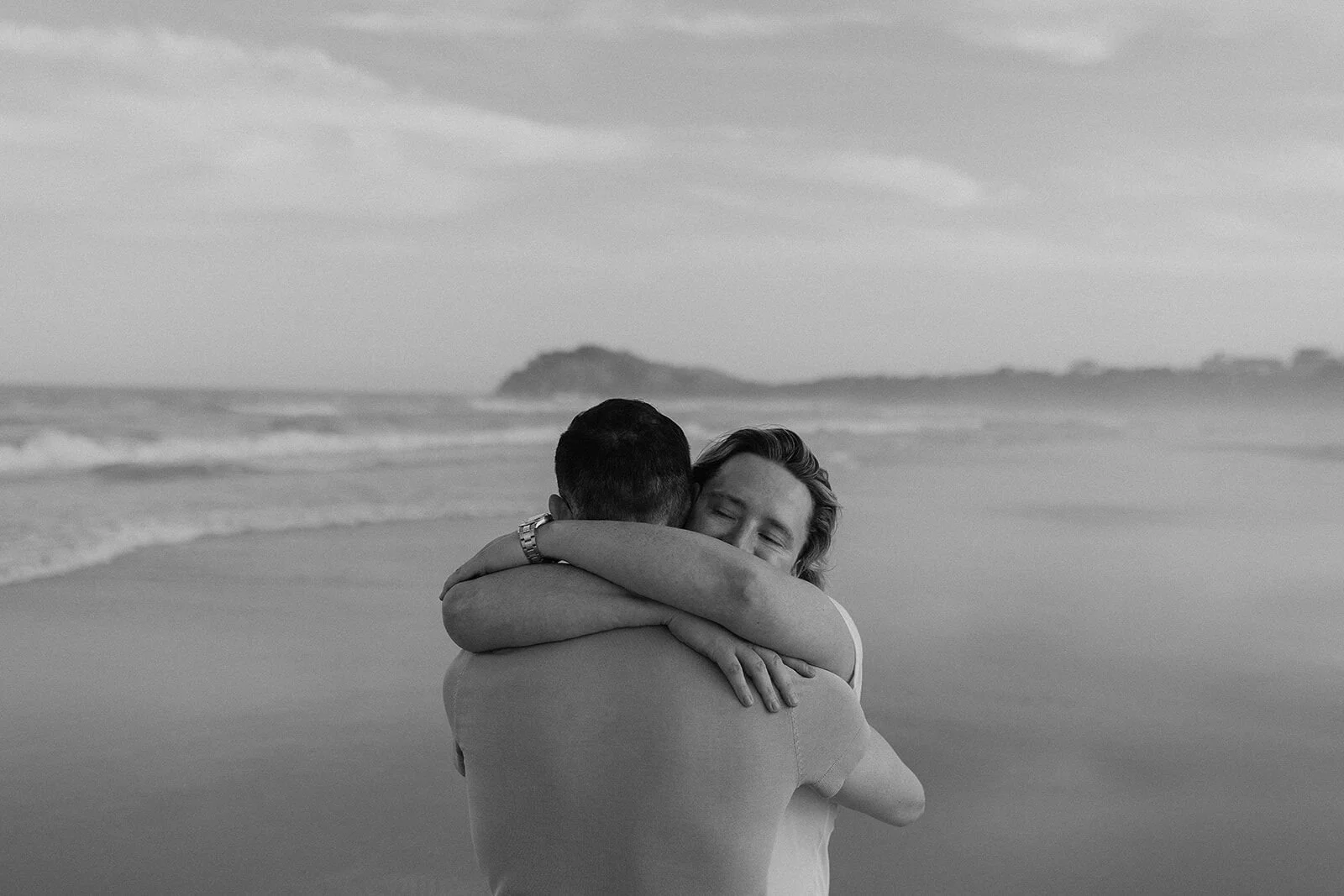 Black and white of the couple hugging at the water's edge, Byron and Luke's marriage proposal at Cabarita Beach, Northern Rivers