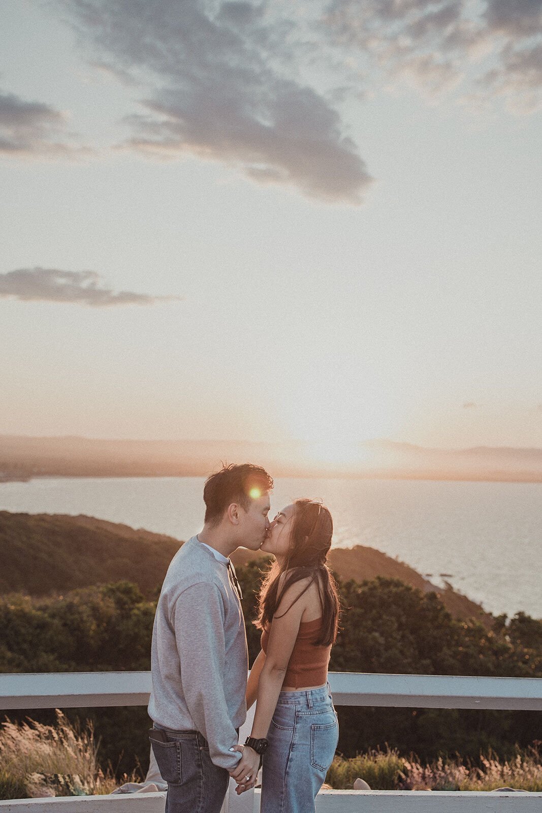 Couple kissing at the lookout railing as the sun sets, Douglas and Ying's sunset marriage proposal at Cape Byron Lighthouse, Byron Bay