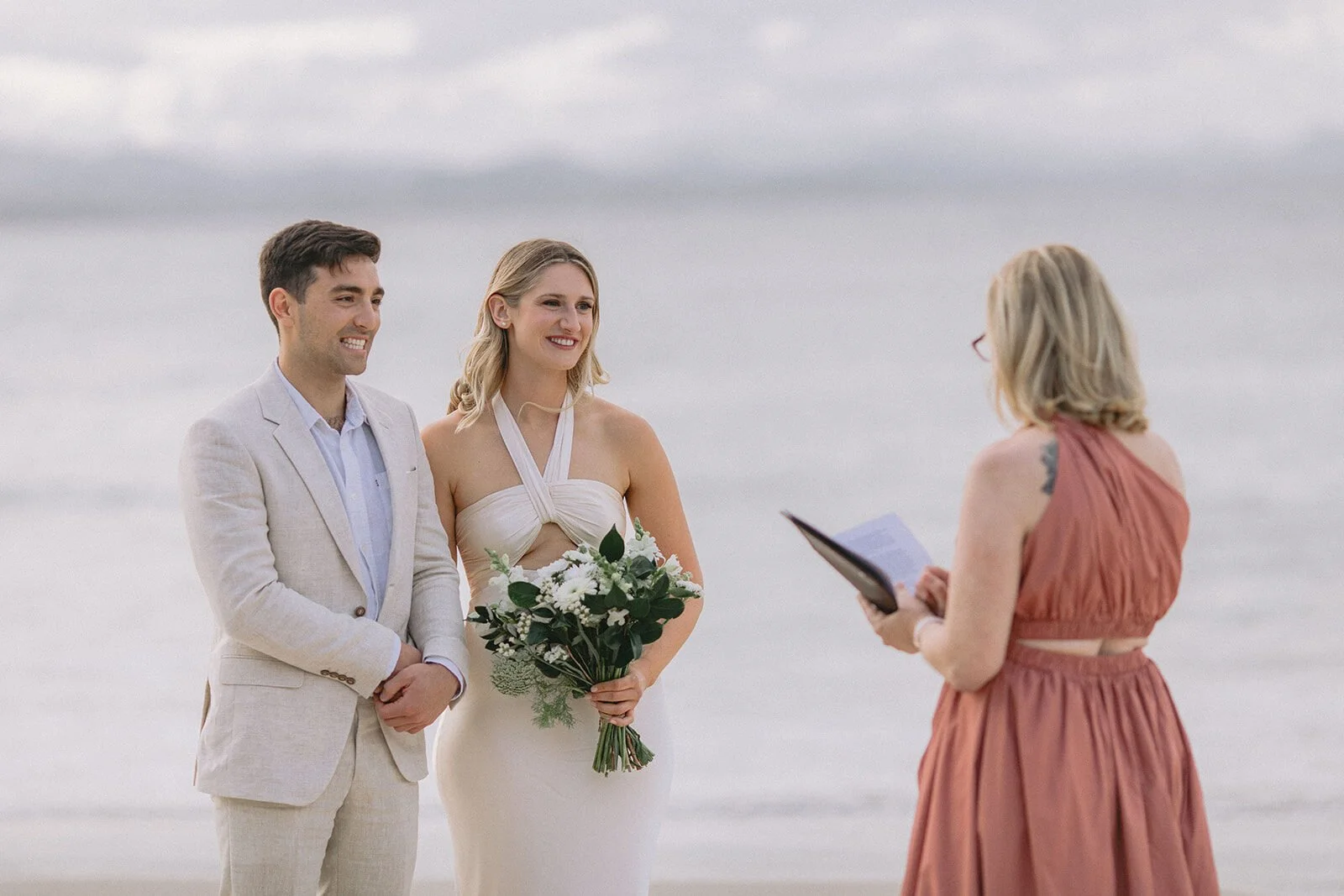 Couple smiling as the celebrant reads their vows, Abby and James' elopement at Little Wategos Beach, Byron Bay