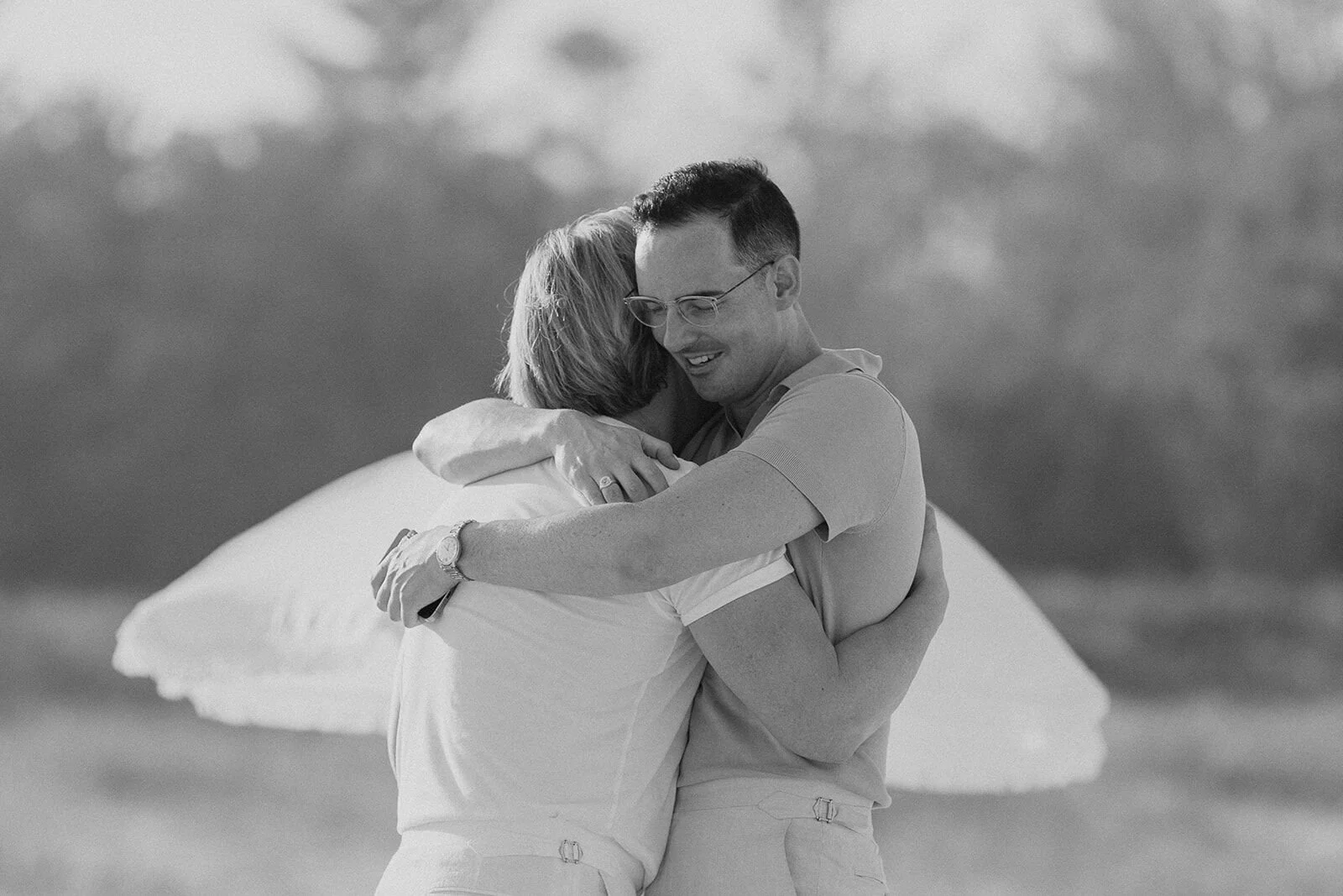 Black and white of the couple hugging beneath a white beach umbrella, Byron and Luke's marriage proposal at Cabarita Beach, Northern Rivers