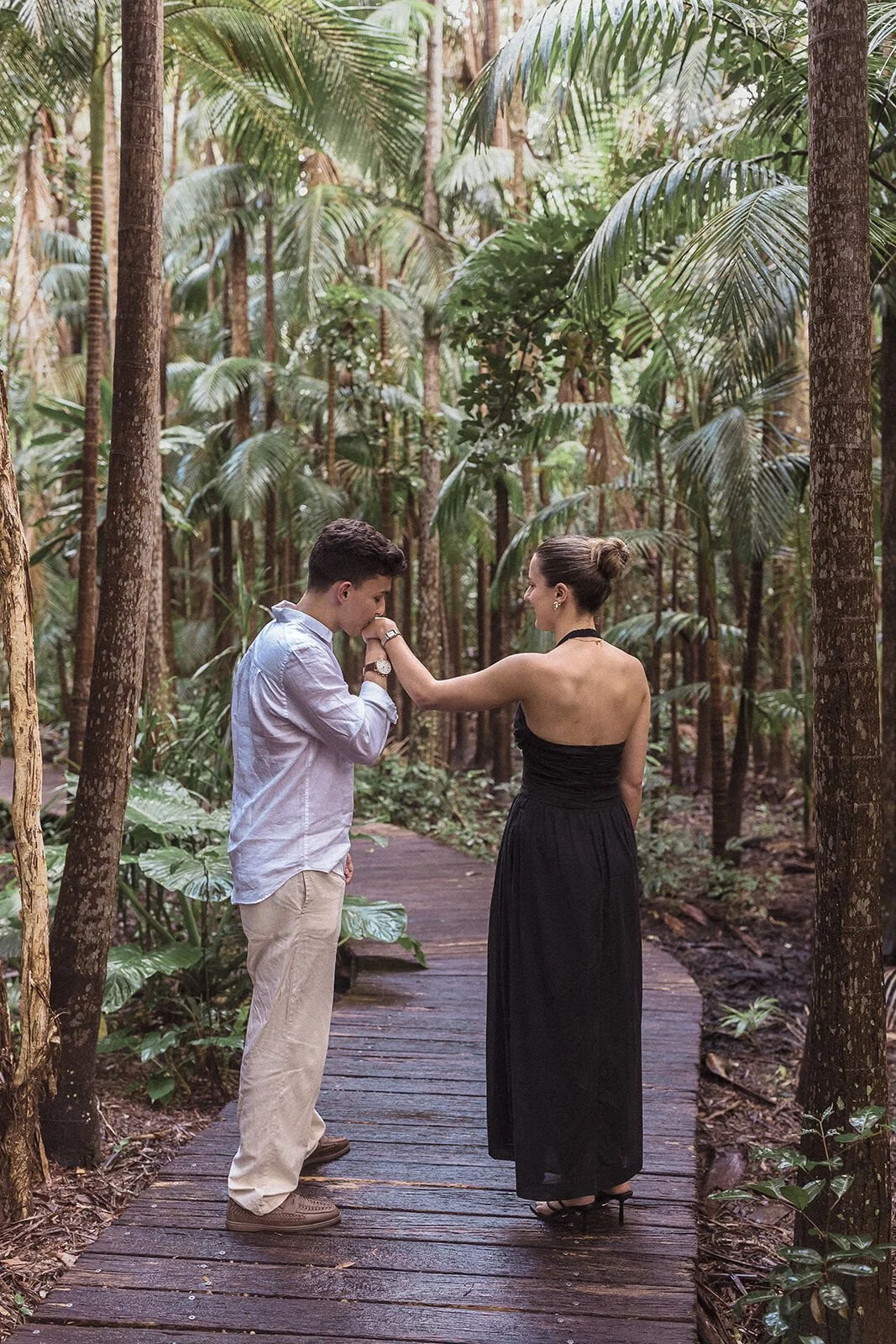 Man kissing his fiancée's hand on the boardwalk, Ben and Chloe's marriage proposal in Byron Bay