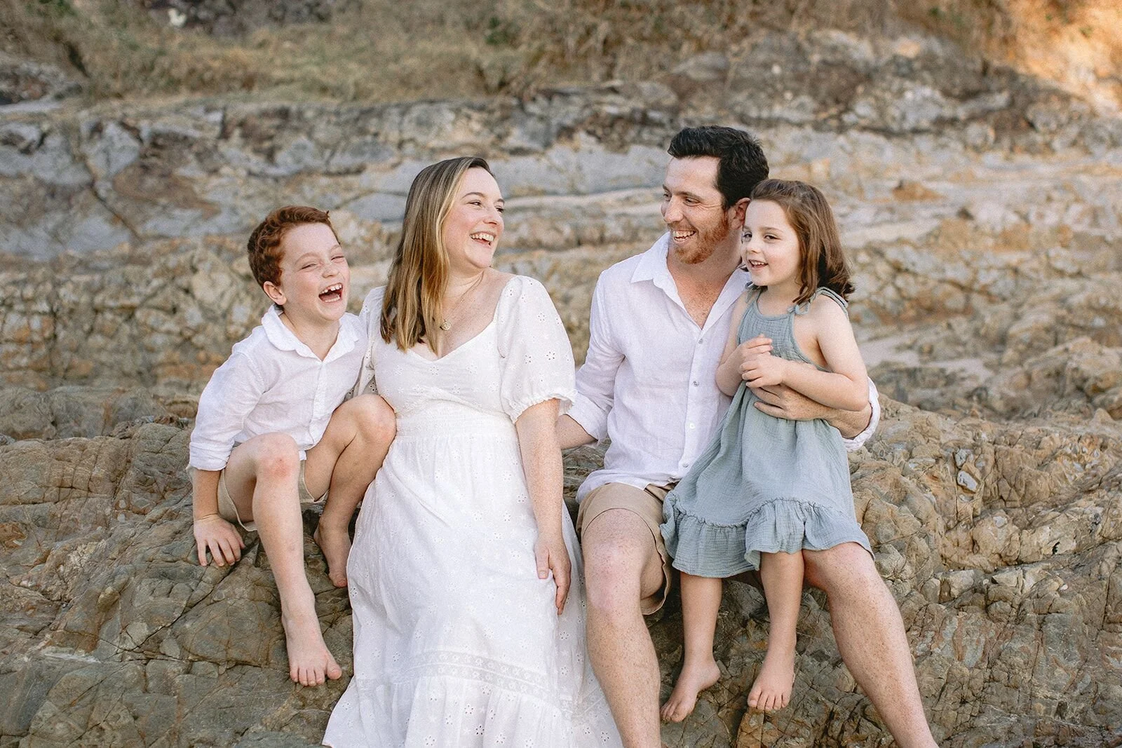 Family of four laughing together on the rocks at The Pass, Byron Bay family photographer