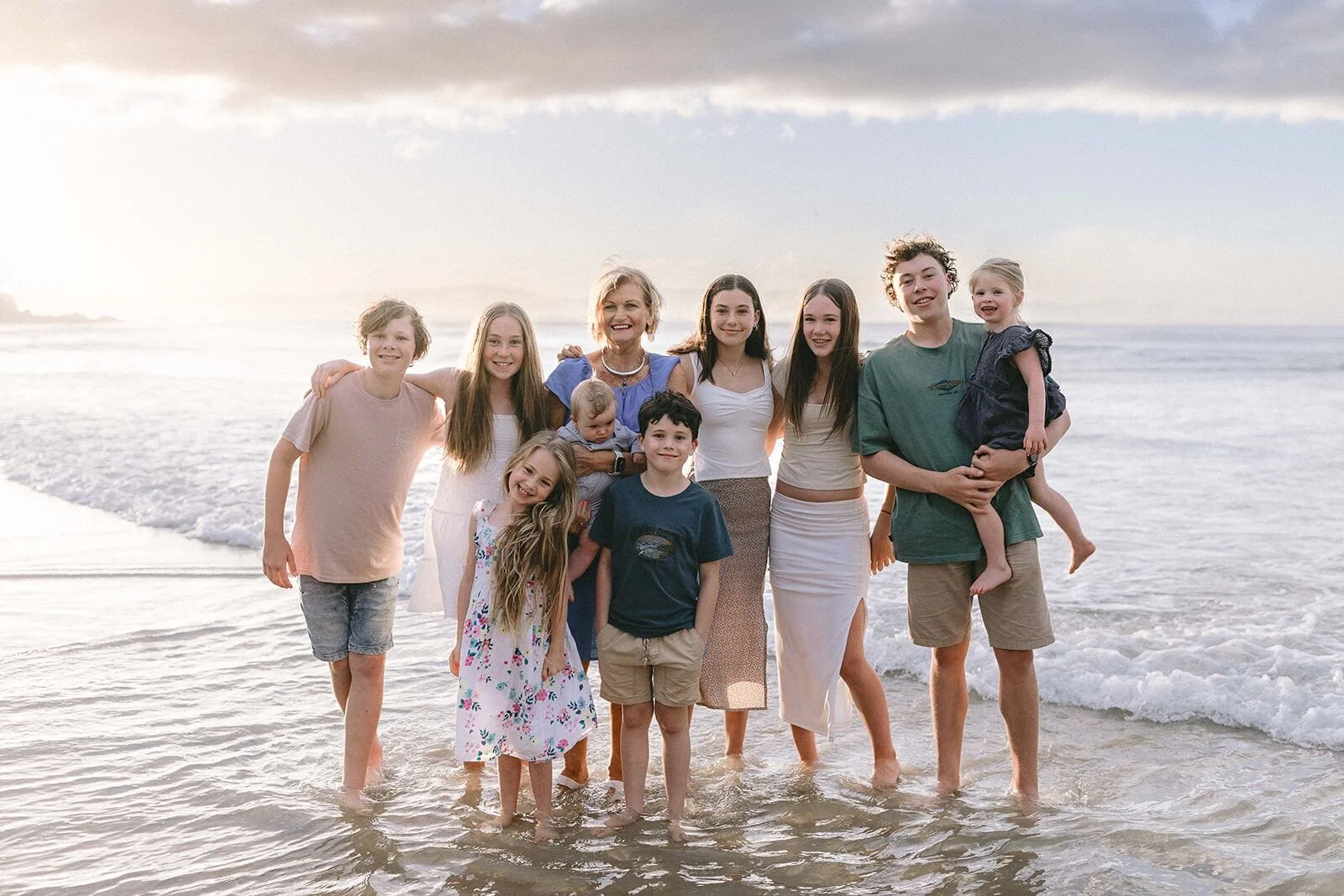 Three generations of one family standing together in the shallows, with a toddler held up high
