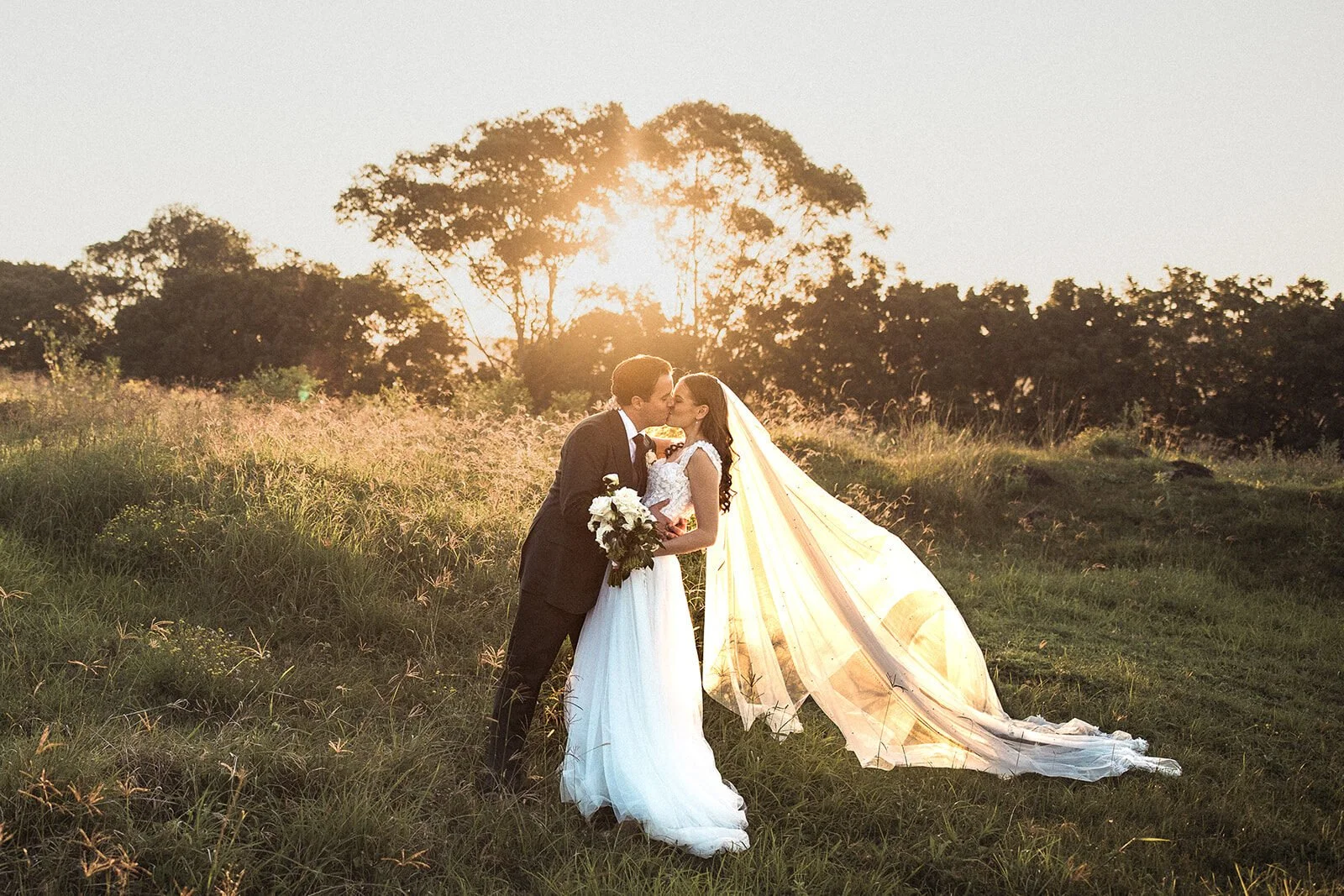 Couple kissing in the sunset with the bride's veil flying, Steph and William's wedding at Earth House, Byron Bay
