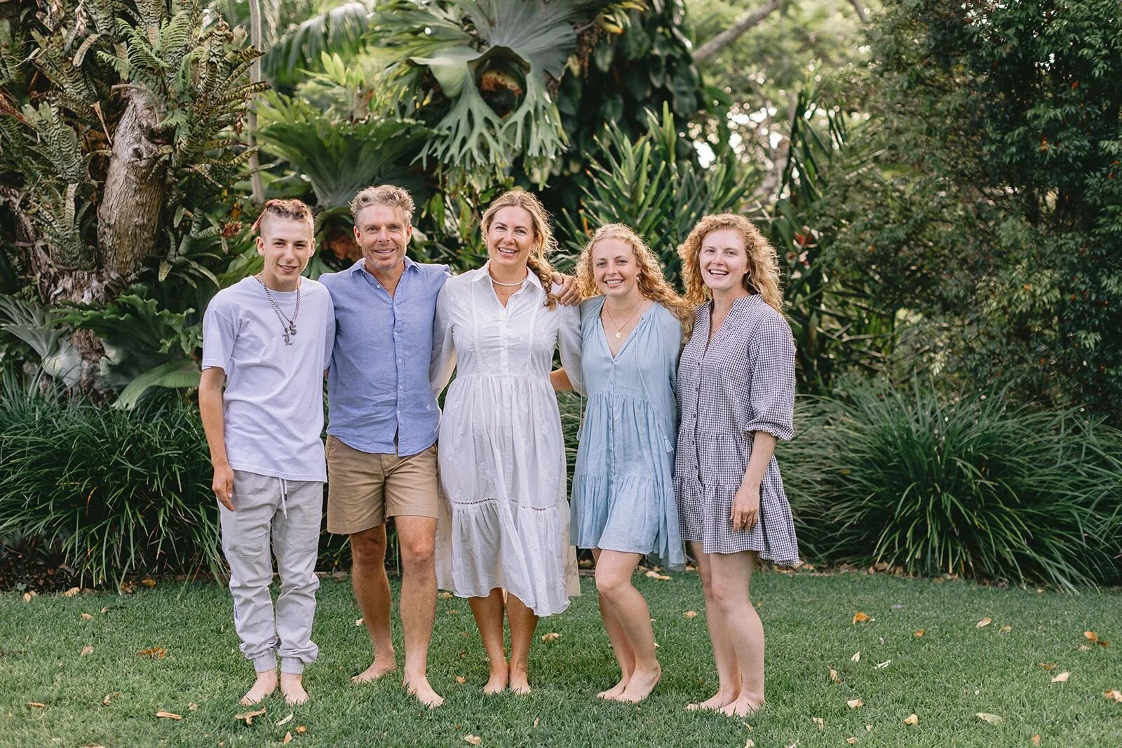Parents and three grown children standing together in a rainforest garden, all smiling