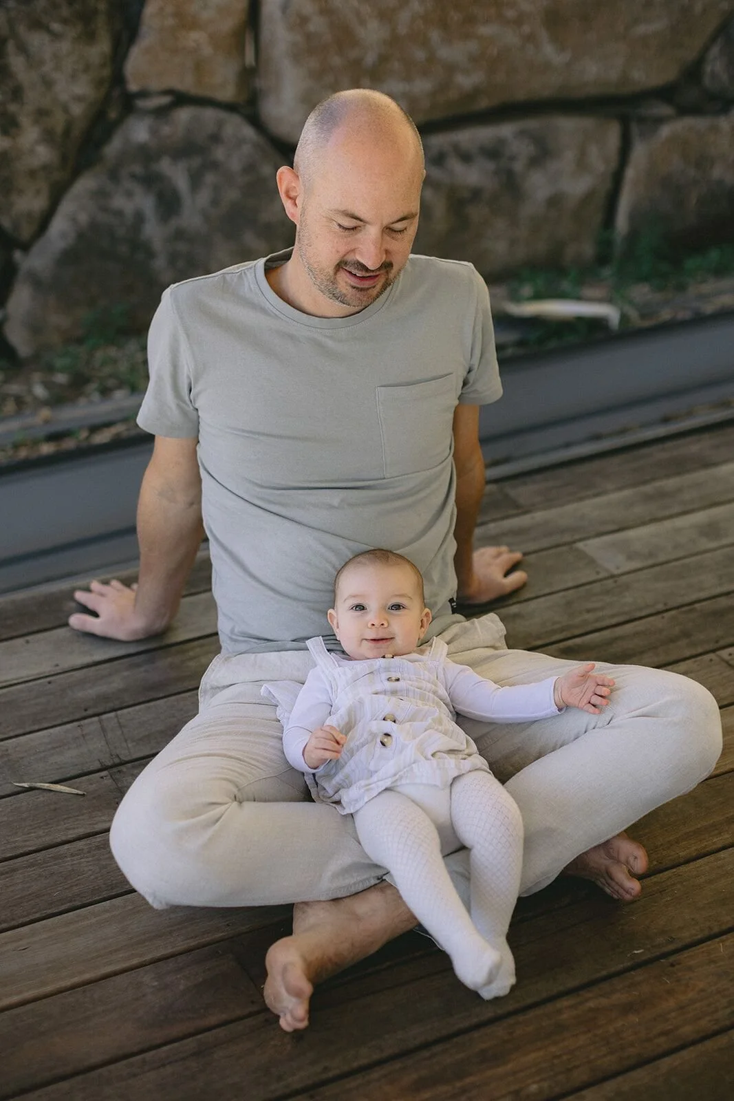 Dad sitting on a timber deck with his baby daughter in his lap