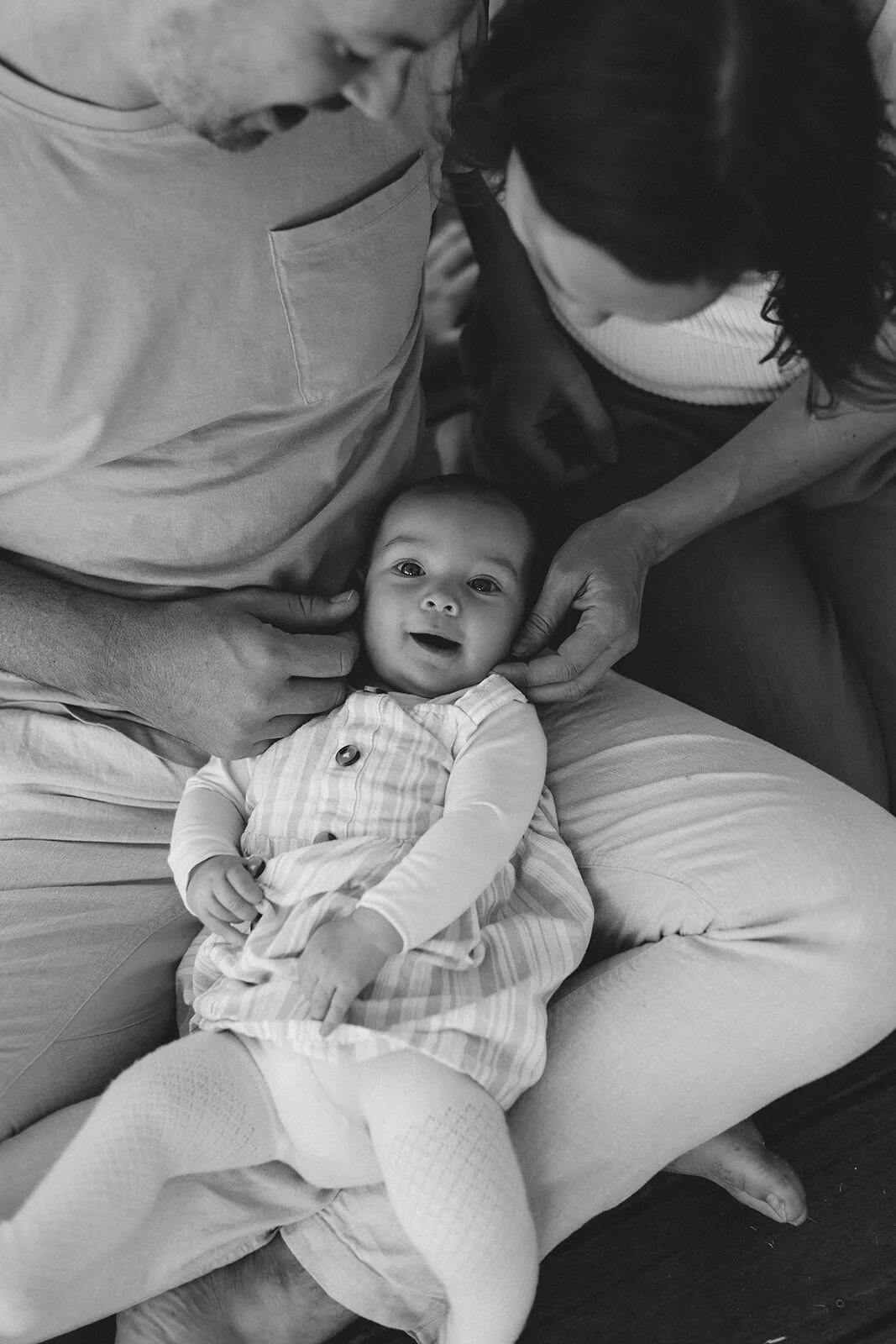 Black and white overhead shot of a baby in her parents' lap as they cradle her face