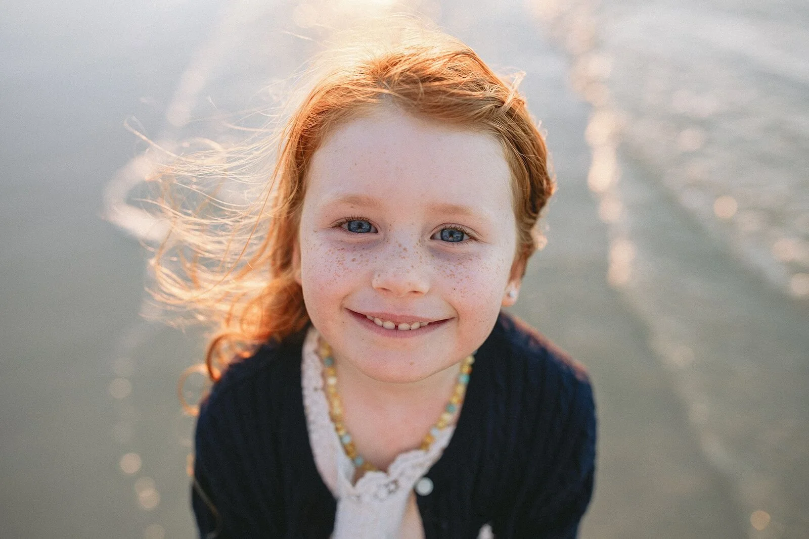 Portrait of a smiling girl with backlit red hair at the water's edge