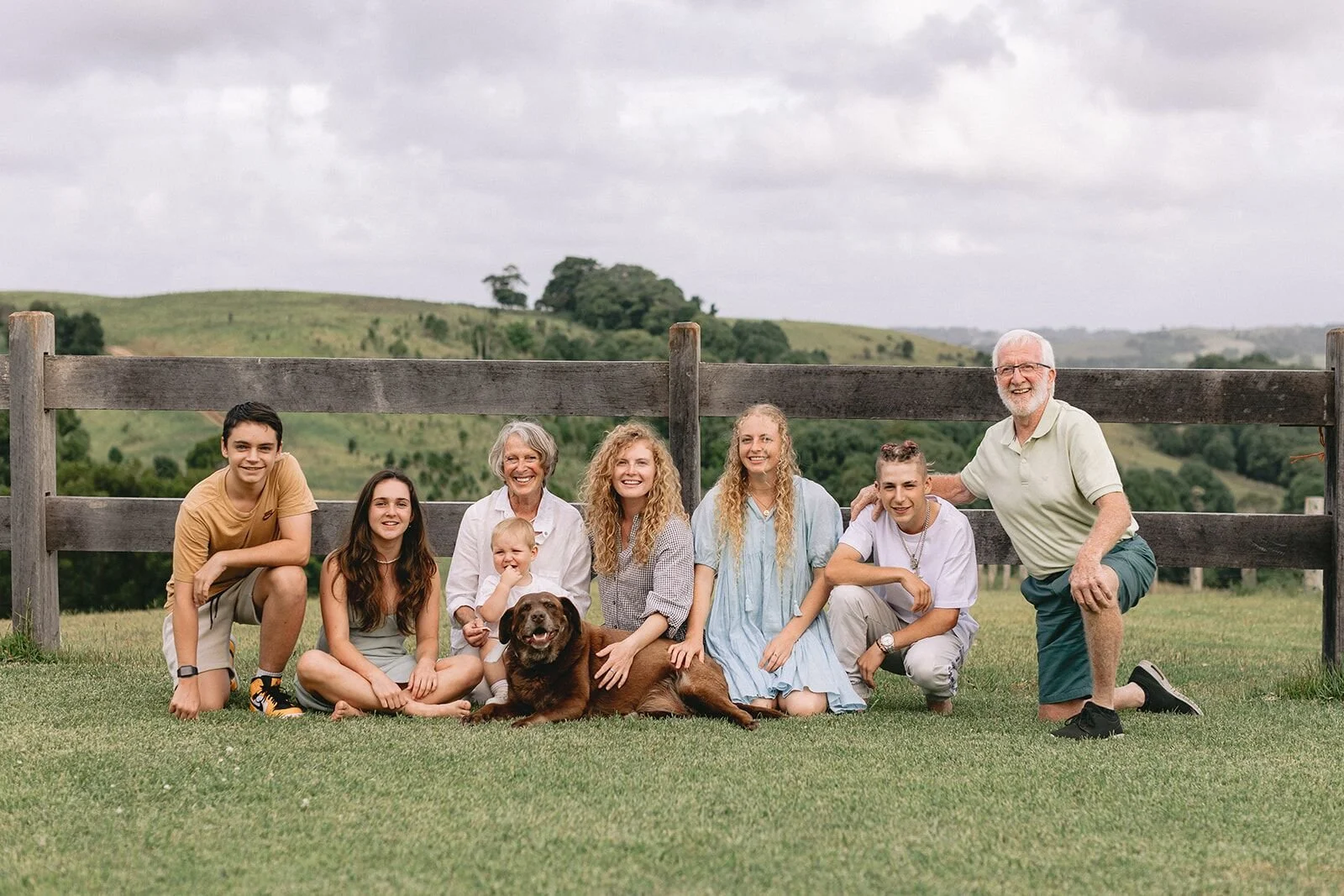 Relaxed family group portrait on the lawn, the dog lying in front, Possum Creek hills behind