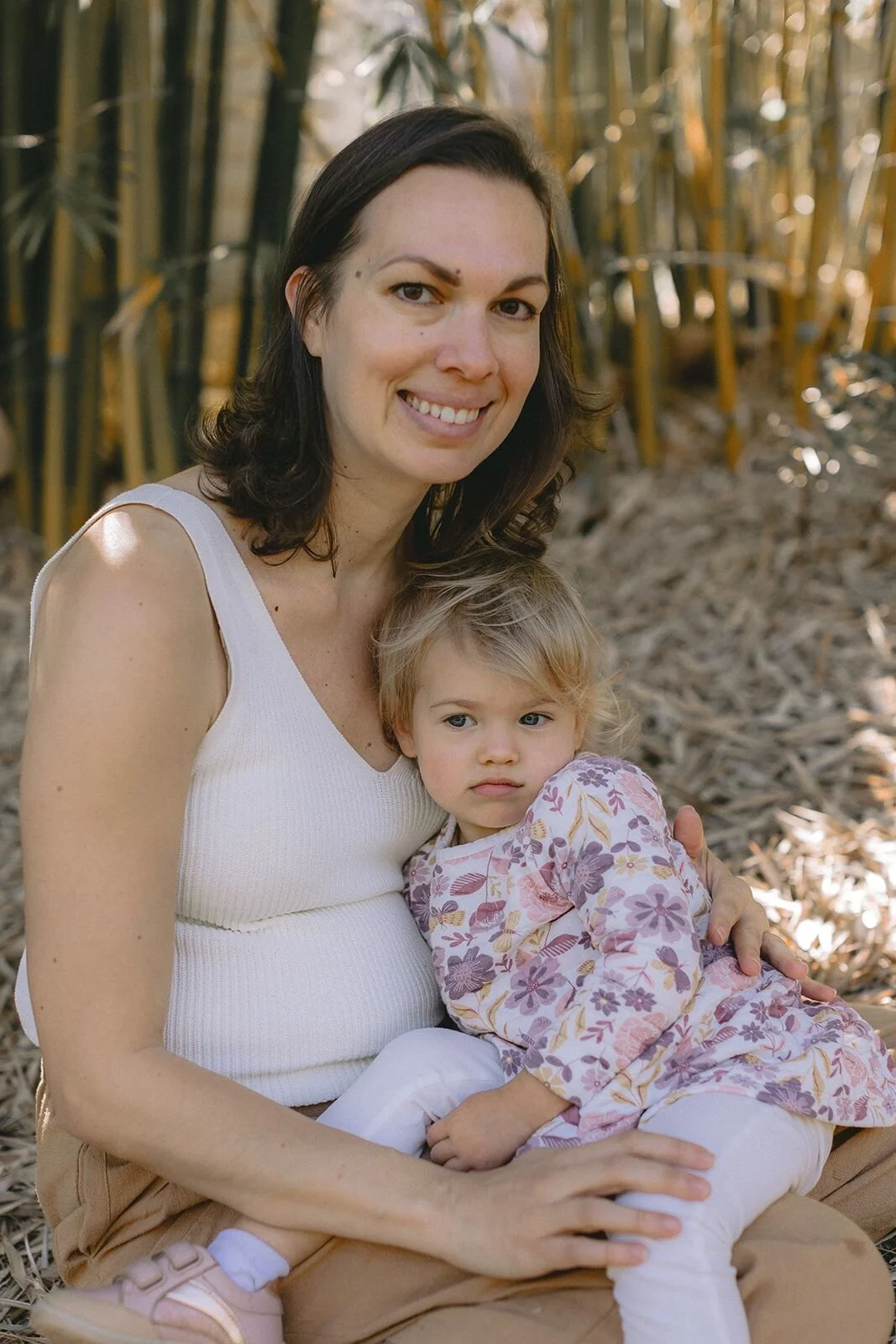 Smiling mum cuddling her toddler on her lap among the bamboo