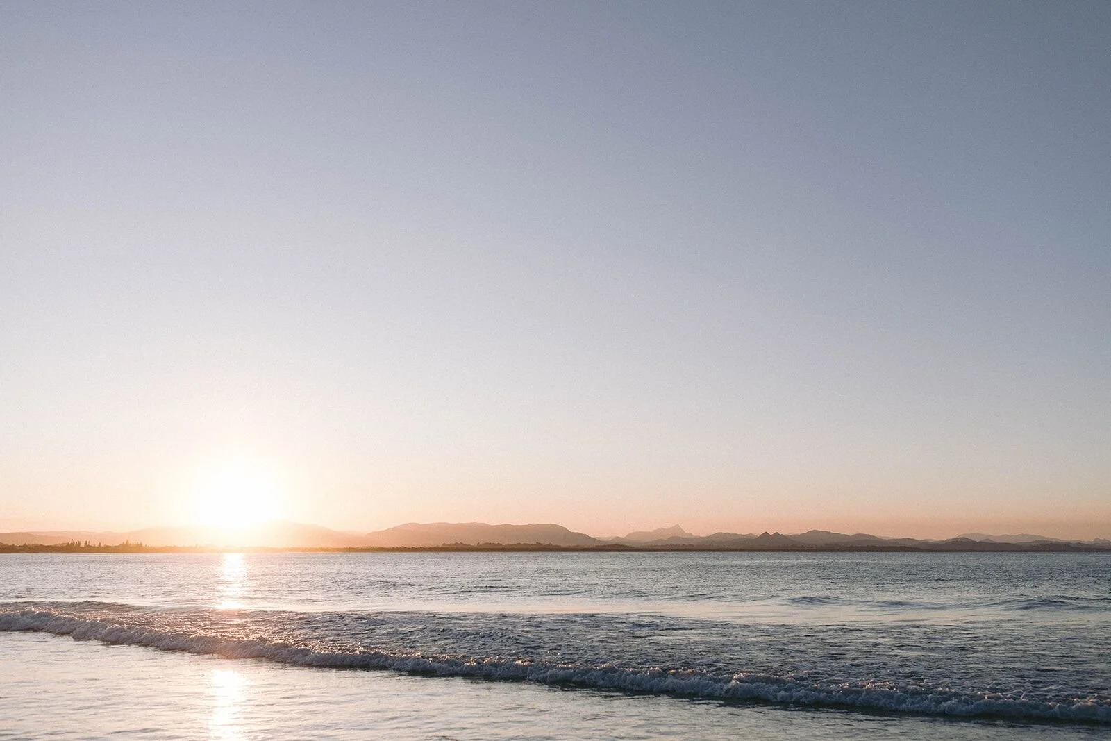 Sun setting over a calm sea and headland at The Pass, Byron Bay