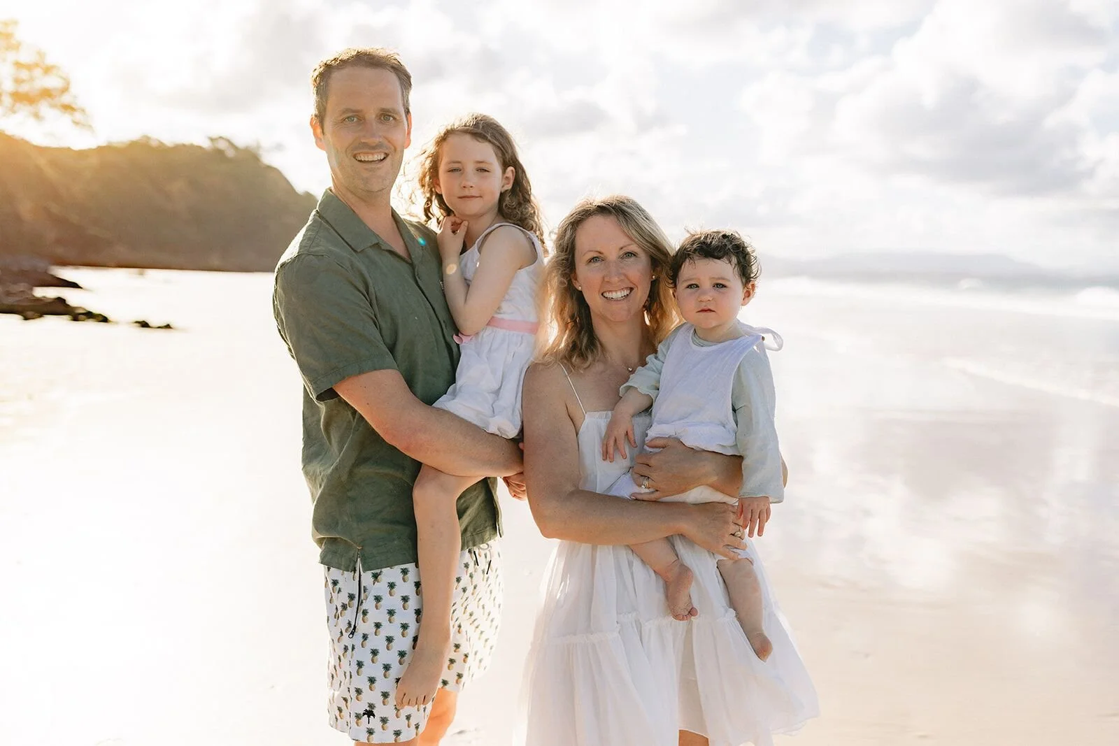Family beach portrait at Wategos with dad holding his daughter and mum holding their toddler son