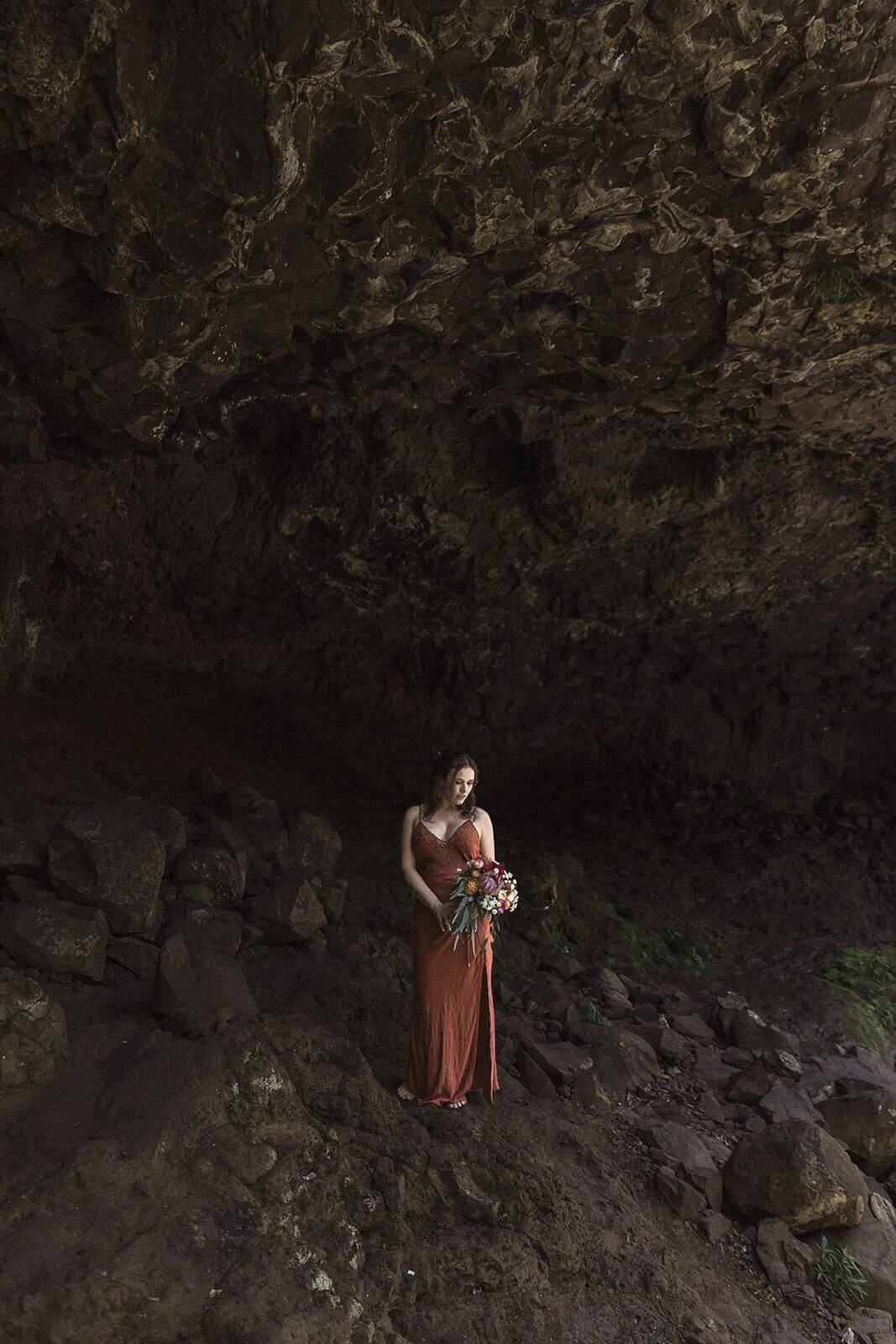 Bride in a rust dress standing alone in the dark cave, Sara and Graeme's elopement at Killen Falls, Northern Rivers