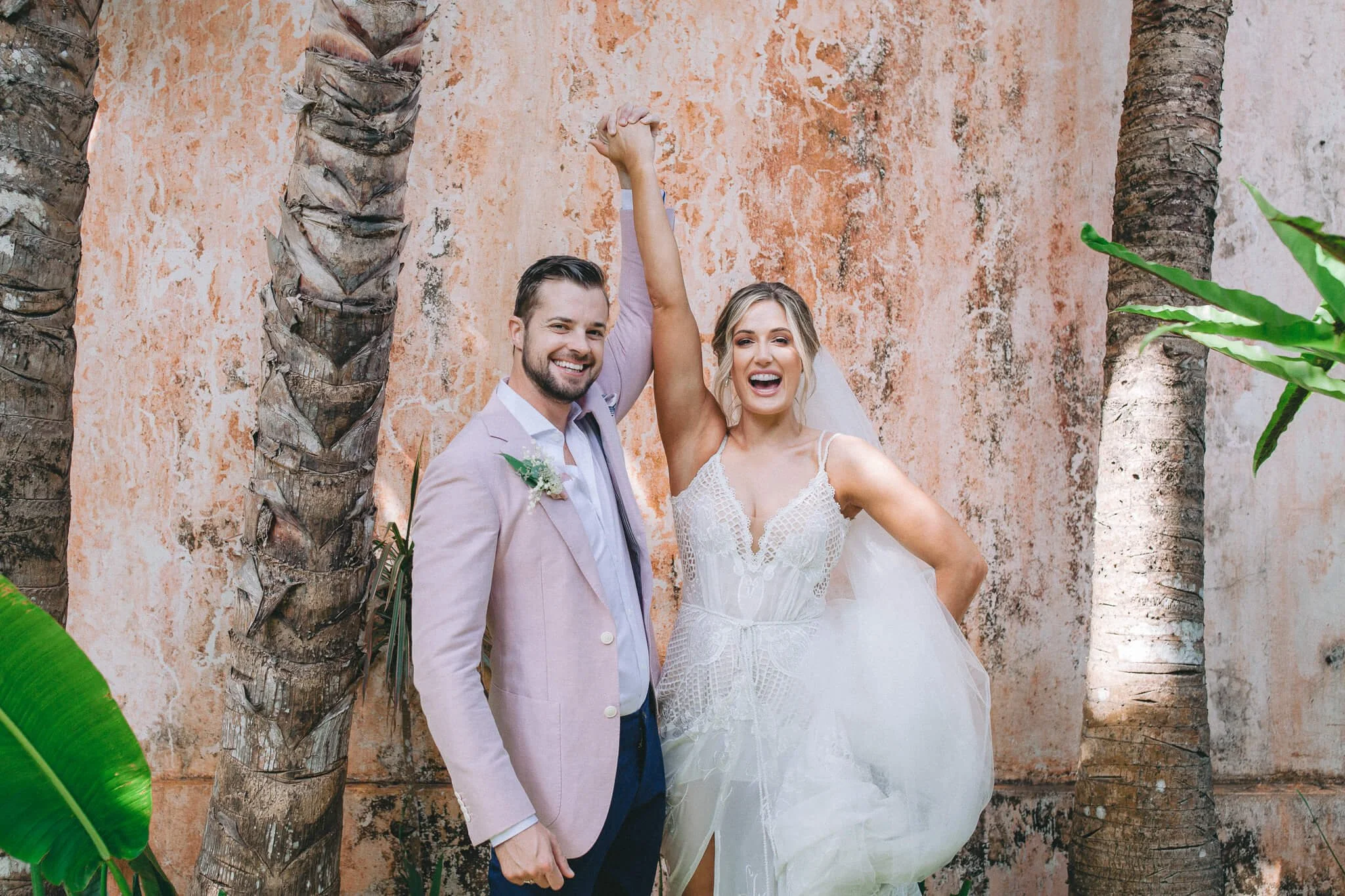 Bride and groom celebrating against a weathered pink wall at Khayangan Estate, Bali