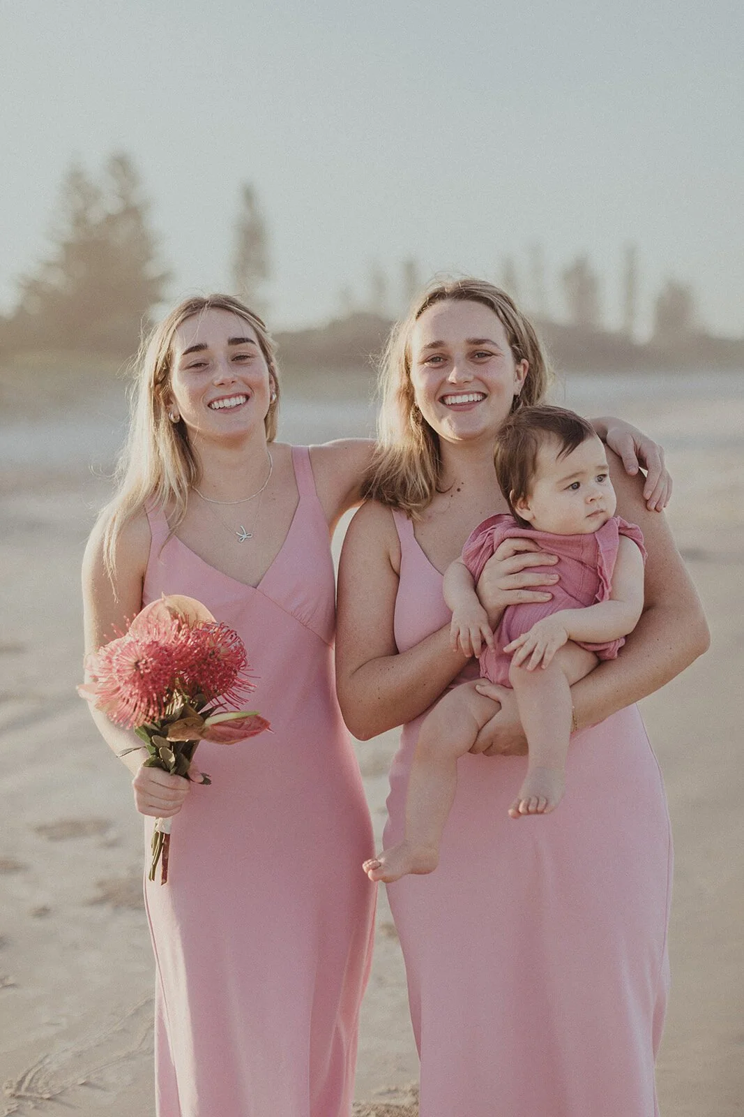 Two young women in pink dresses laughing while holding the baby, Maritess and Mark's elopement at Lennox Head