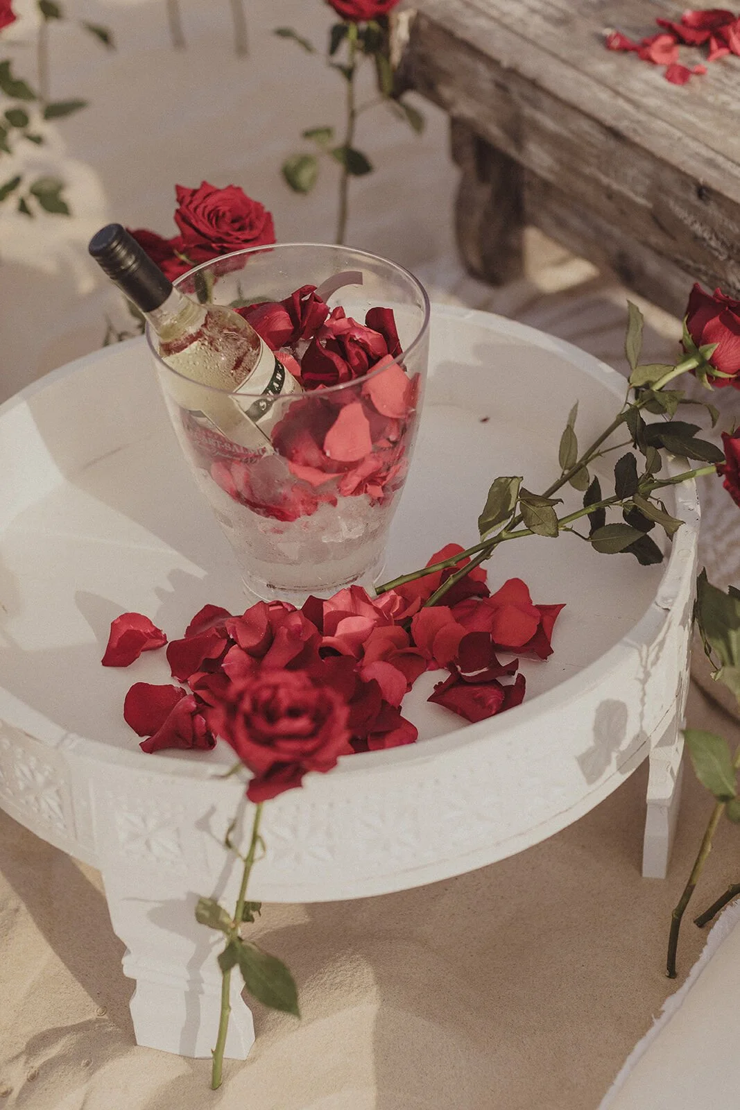 White tray holding a glass bucket of champagne and red roses on the sand, Byron and Luke's marriage proposal at Cabarita Beach, Northern Rivers