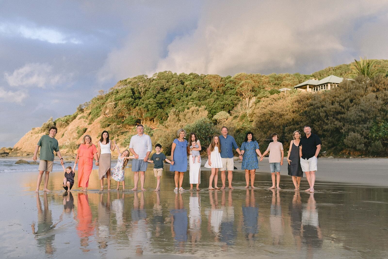 Extended family holding hands in a line on the beach, reflected in the wet sand at sunset