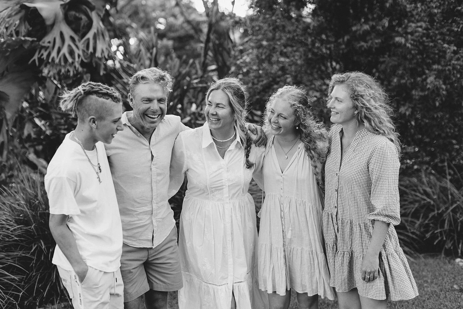 Black and white portrait of parents and their grown children arm in arm among tropical plants