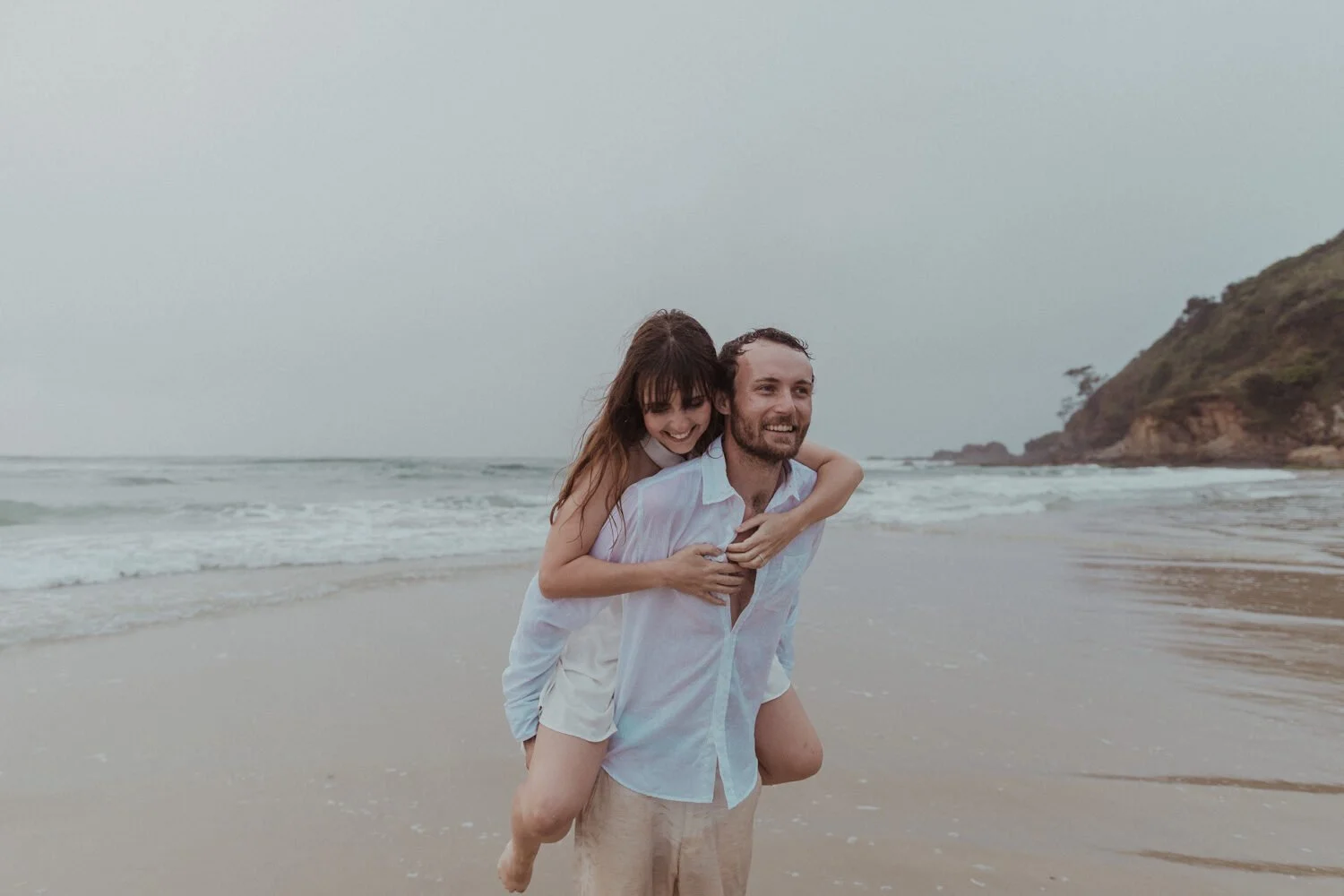 Groom giving the bride a piggyback on the beach, Yoanne and Elisa's rainy elopement at Broken Head, Byron Bay