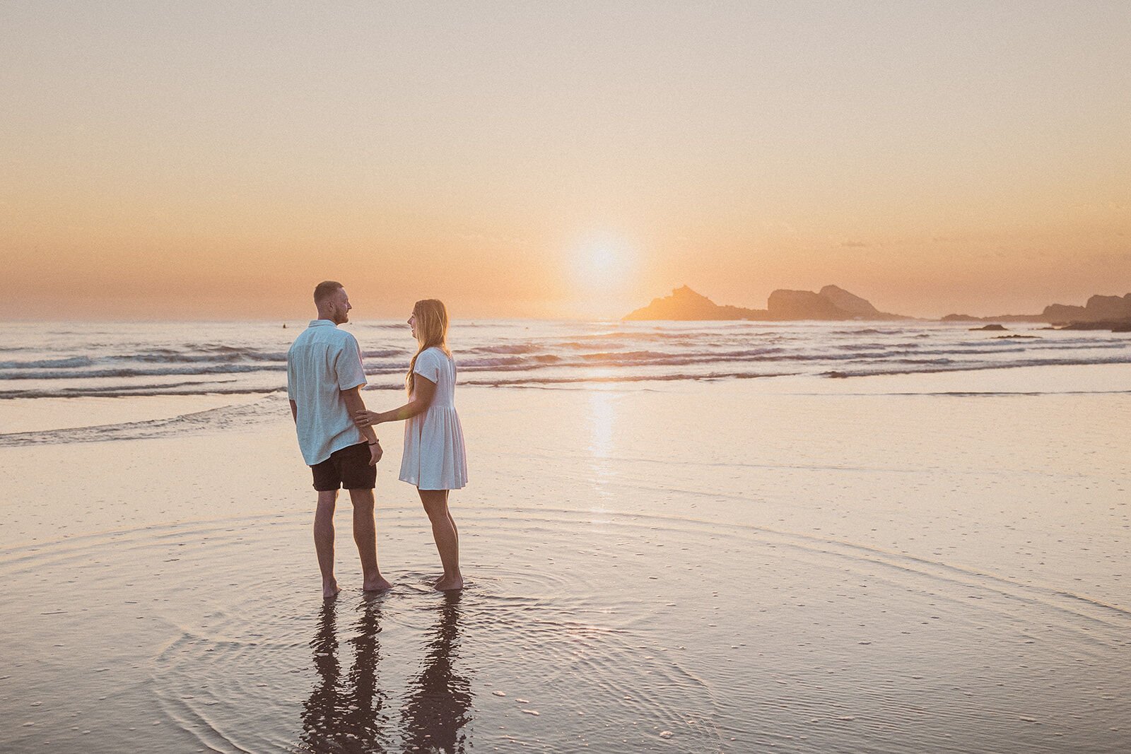 Couple standing in the shallows at sunrise with reflections in the wet sand, Charlie and Hannah's sunrise marriage proposal at Broken Head Beach, Byron Bay
