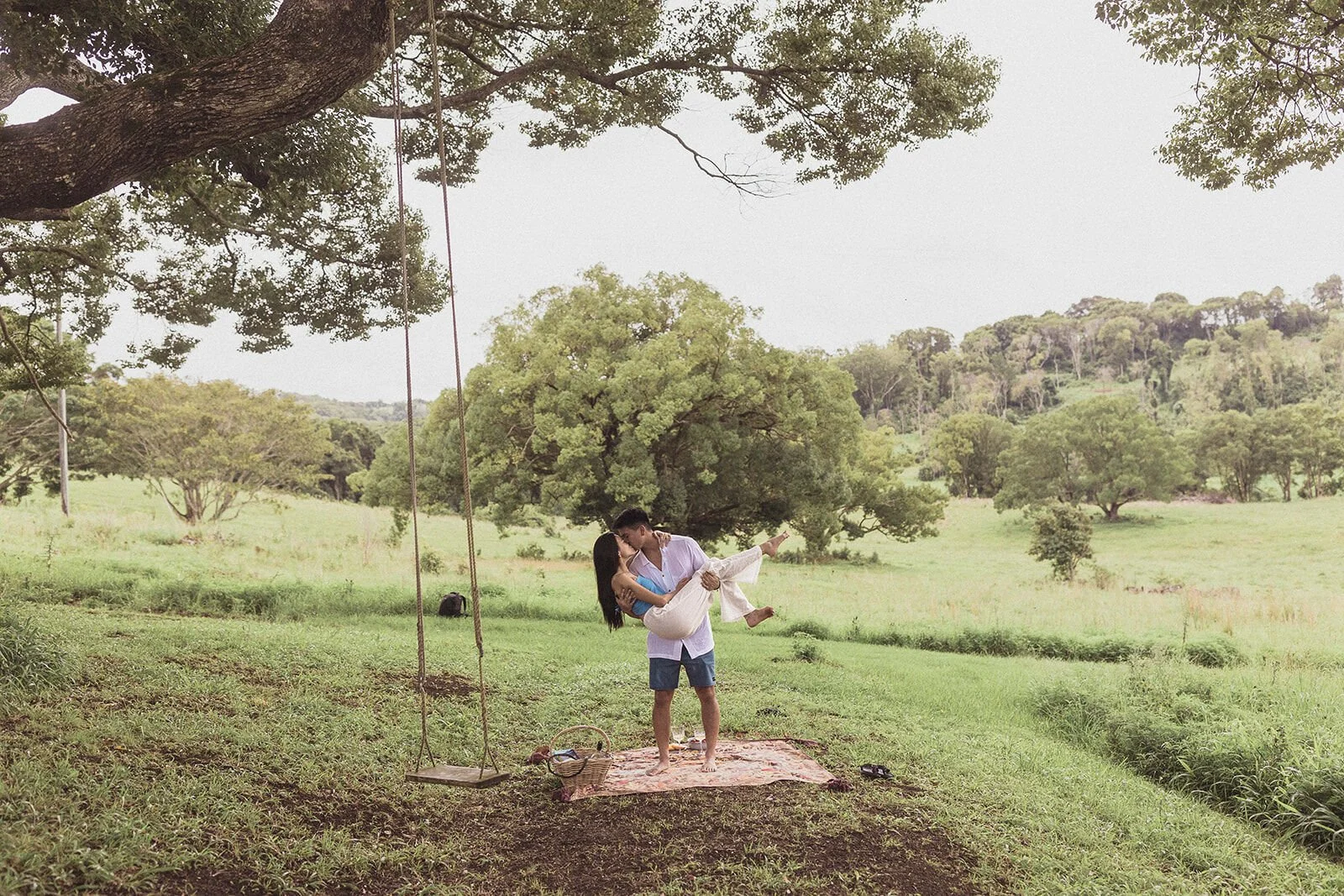 Wide view of the couple under the fig tree and rope swing, Darien and Jacqui's picnic marriage proposal at Heartwood Farm, Byron Bay hinterland