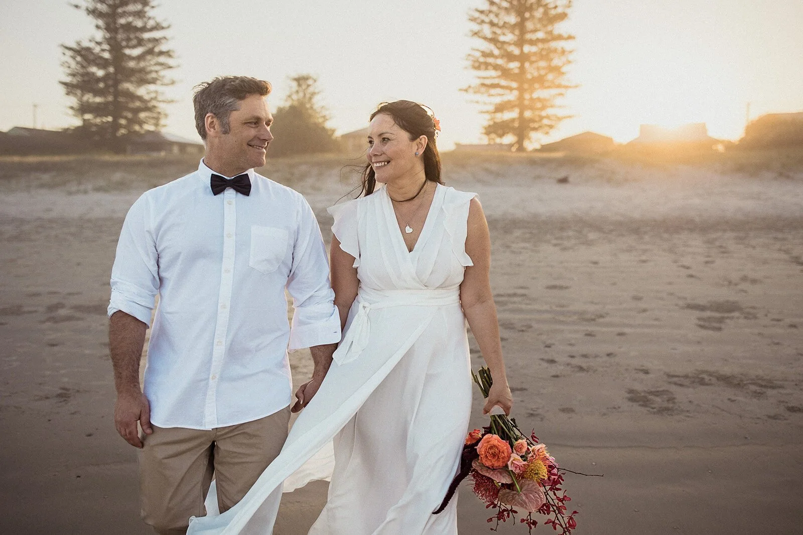 Couple smiling as the bride's white dress blows in the breeze, Maritess and Mark's elopement at Lennox Head