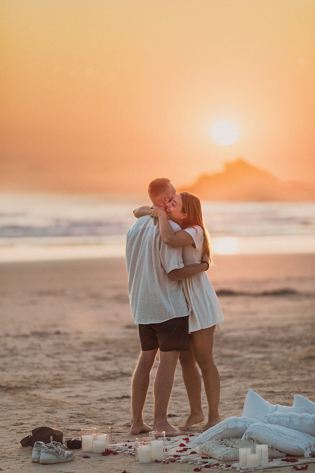 Couple hugging and kissing in front of the rising sun, Charlie and Hannah's sunrise marriage proposal at Broken Head Beach, Byron Bay