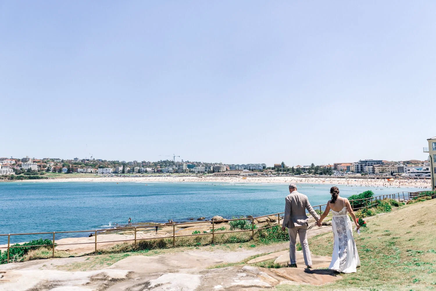Couple walking across the rocks at Ben Buckler with Bondi Beach behind