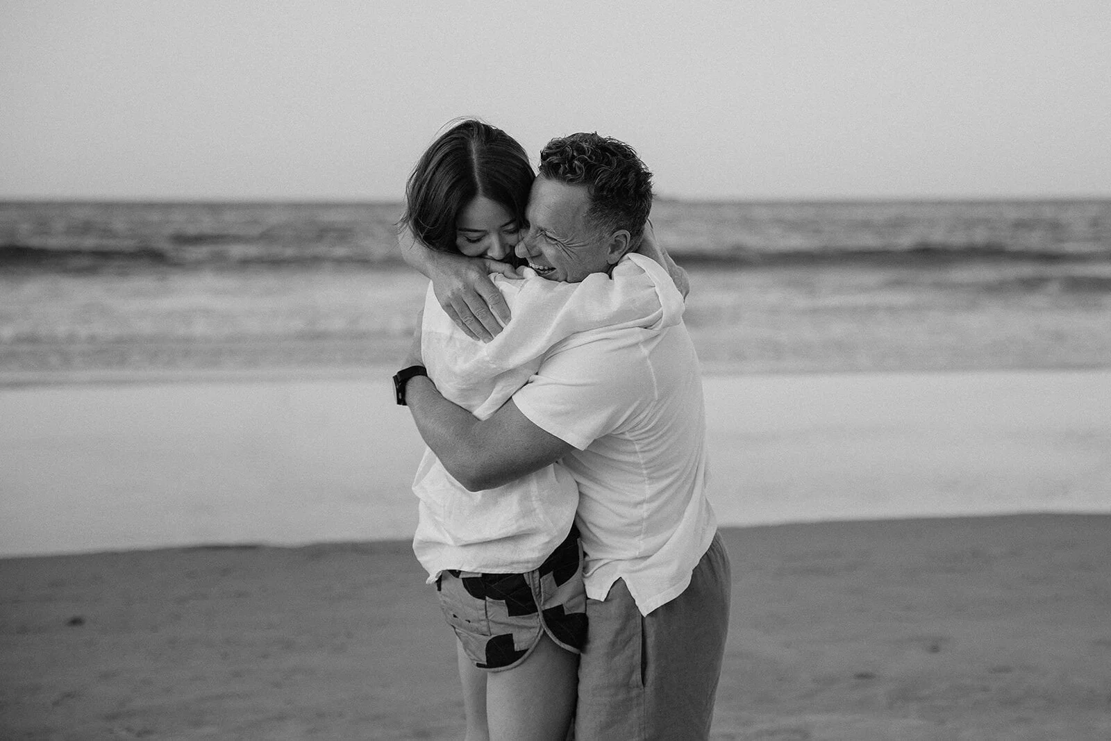 Black and white of the couple hugging tightly, Jamie and Jessica's beach marriage proposal at Belongil Beach, Byron Bay