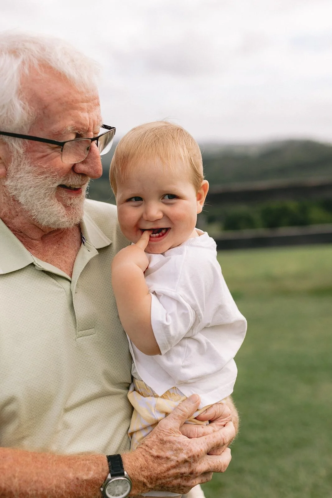 Grandfather in glasses holding his giggling baby grandson, finger in his mouth