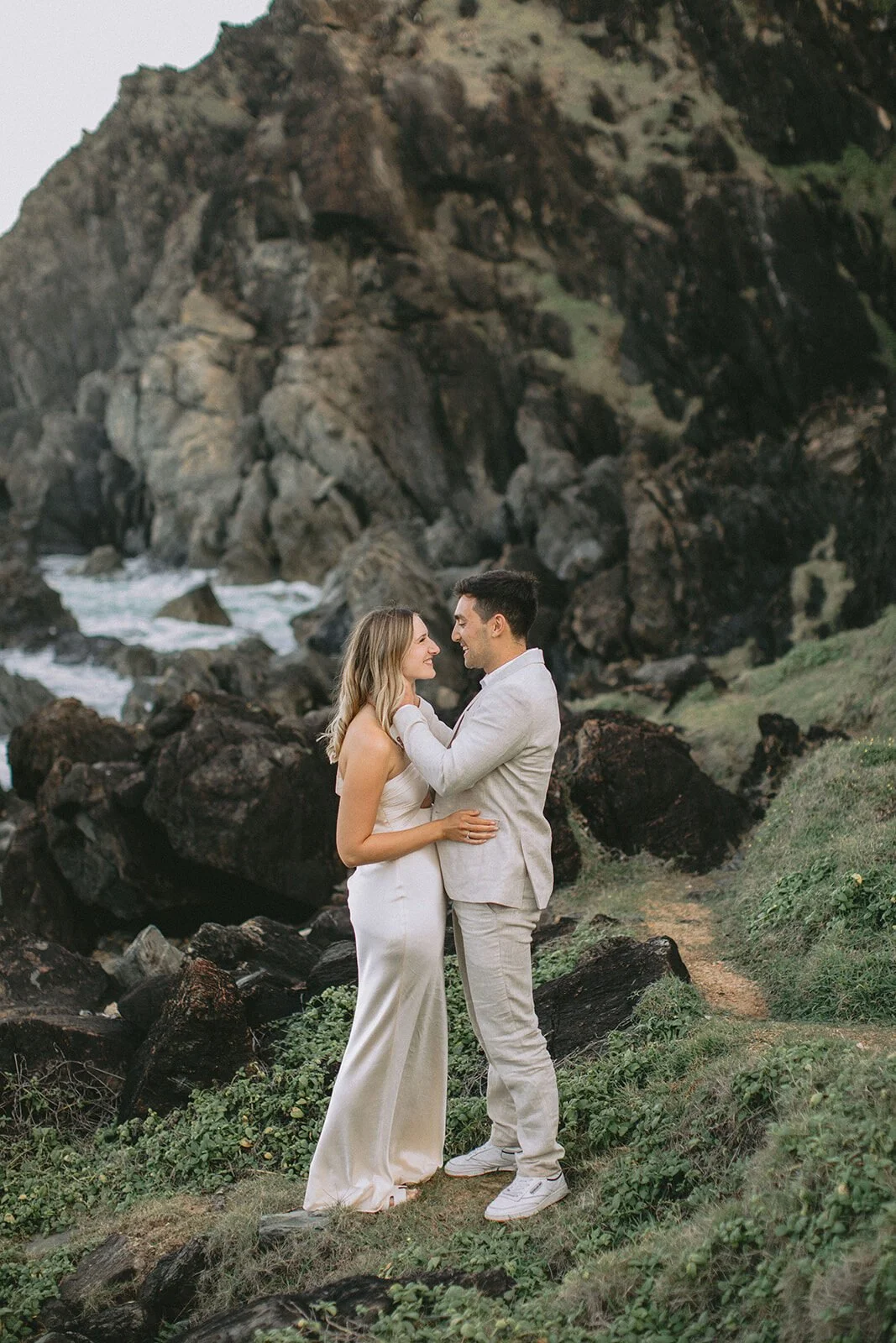 Couple embracing on the grassy rocks above the crashing waves, Abby and James' elopement at Little Wategos Beach, Byron Bay