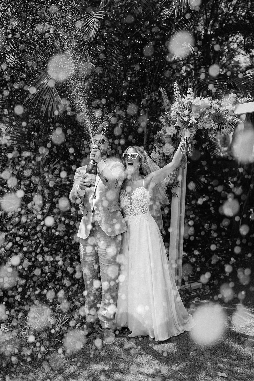 Black and white of the couple spraying champagne, Eliza and Greg's elopement at Broken Head, Byron Bay