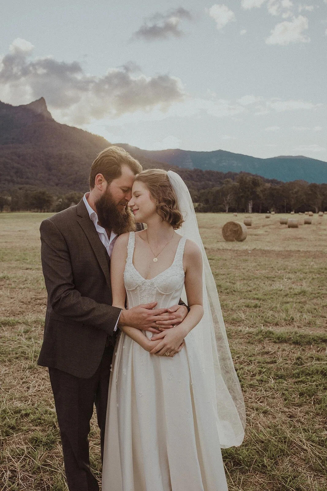 Couple embracing with mountains and hay bales, Sam and Tom's elopement at Highfield Farm, Northern Rivers