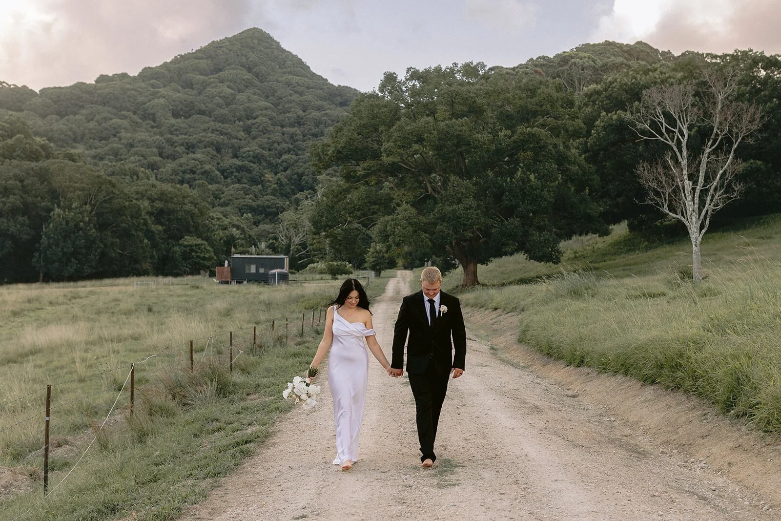 Couple walking along the dirt road with the mountain behind, Kobi and Darren's elopement at Butterfly Lane, Byron Bay hinterland