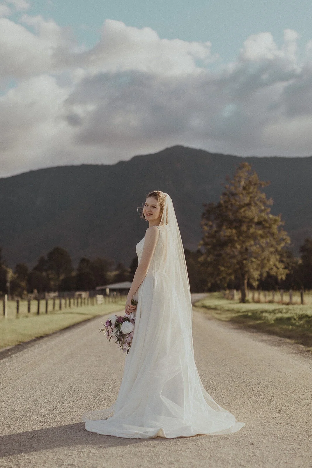 Bride looking over her shoulder on the road, Sam and Tom's elopement at Highfield Farm, Northern Rivers