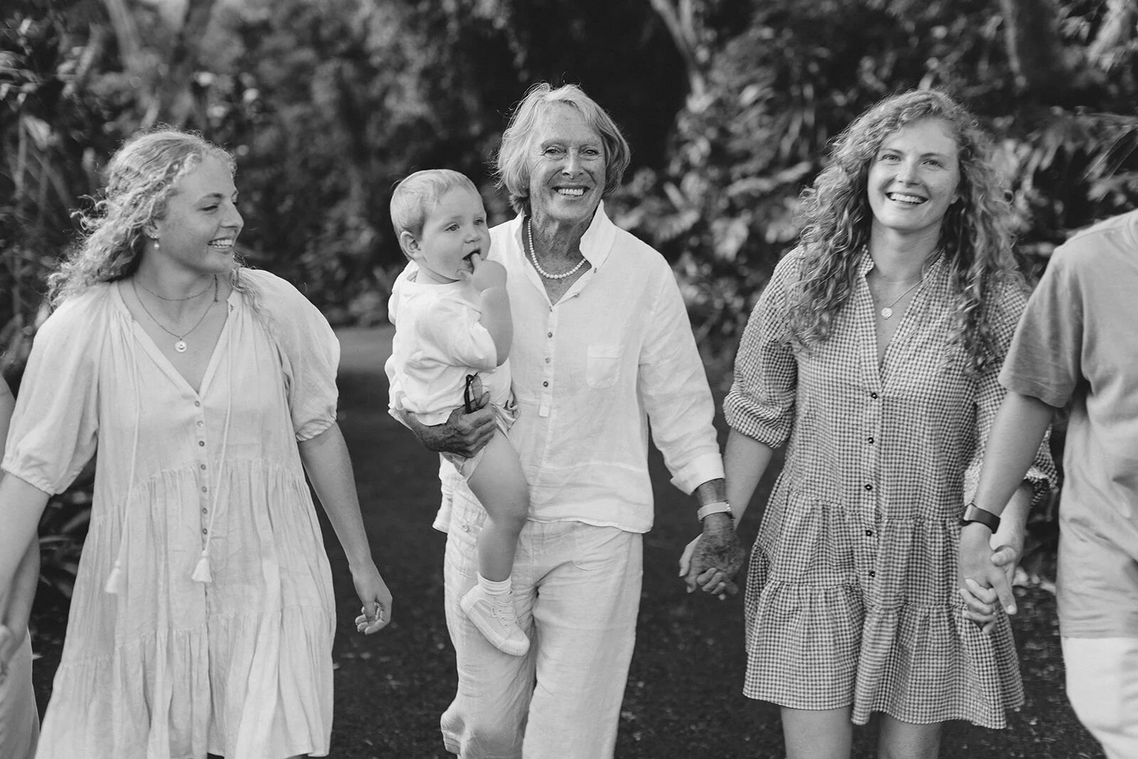 Black and white photo of a grandmother carrying her baby grandson, holding hands with her granddaughters