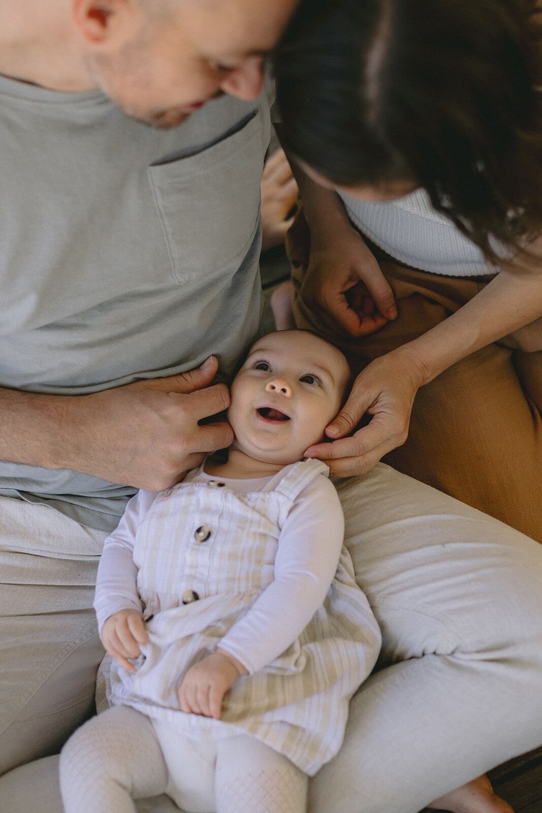 Baby girl smiling up at mum and dad as they hold her face gently