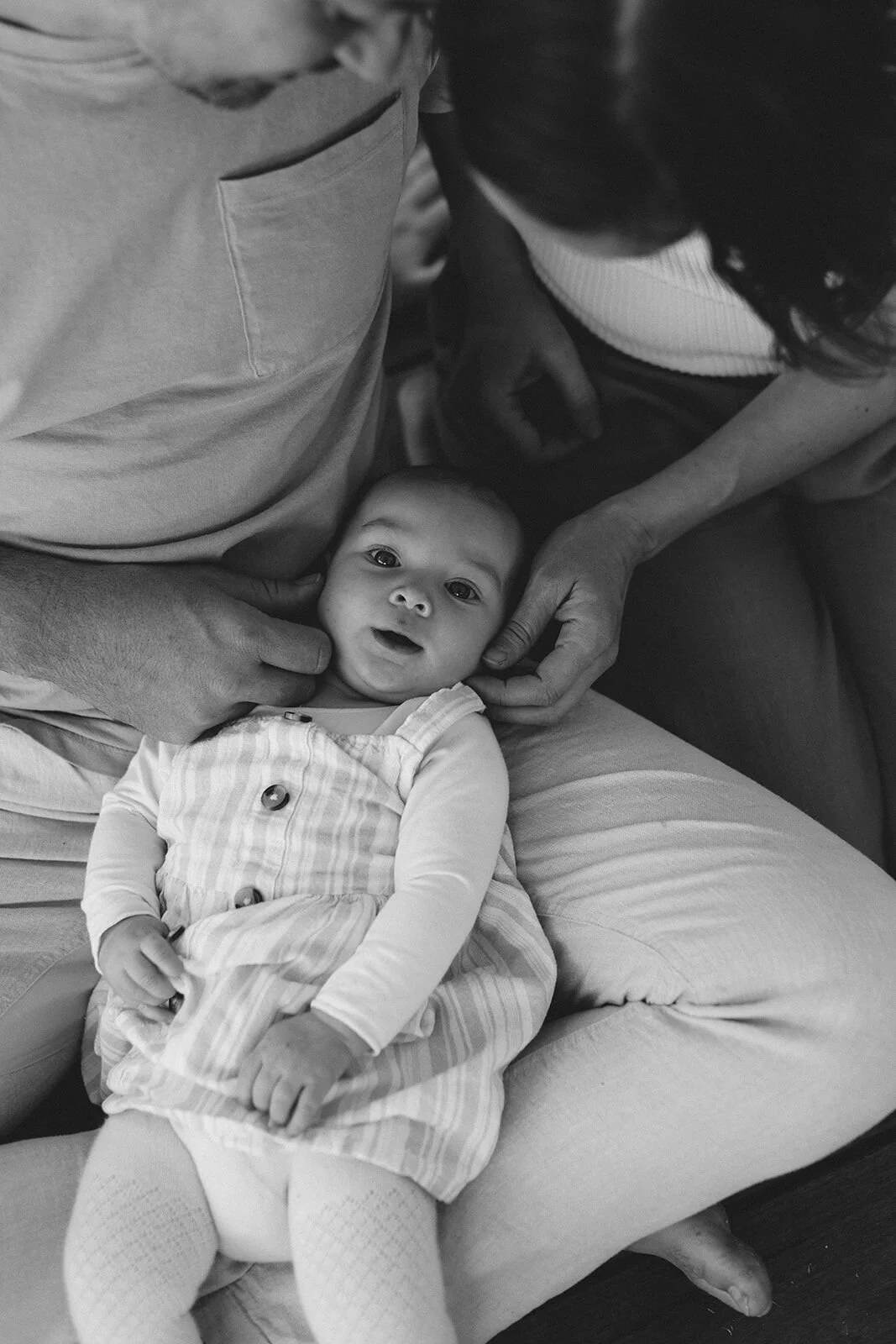 Black and white photo of a baby resting in her parents' laps, hands on her cheeks