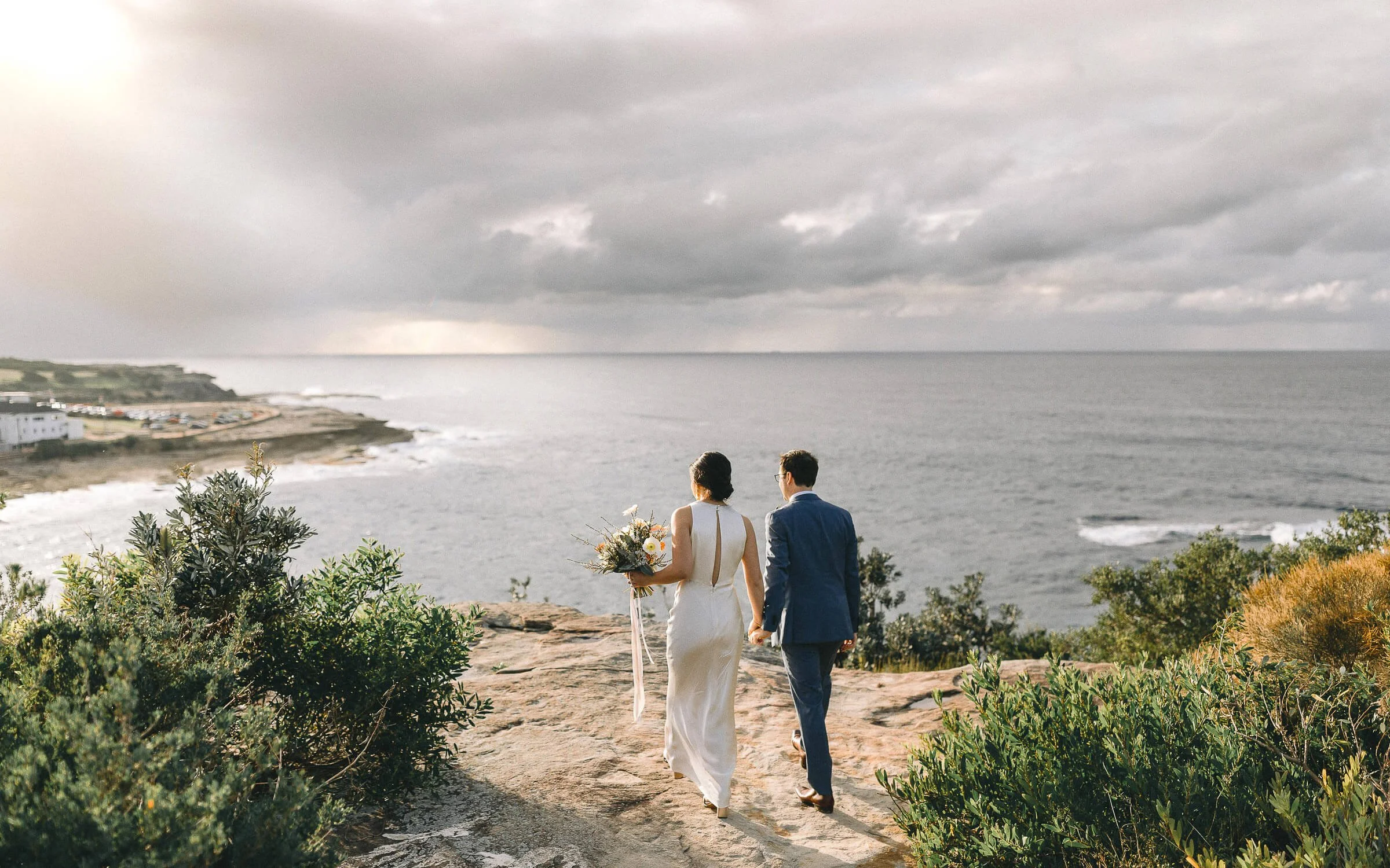 Bride and groom walking the clifftop above the ocean at Coogee, Sydney