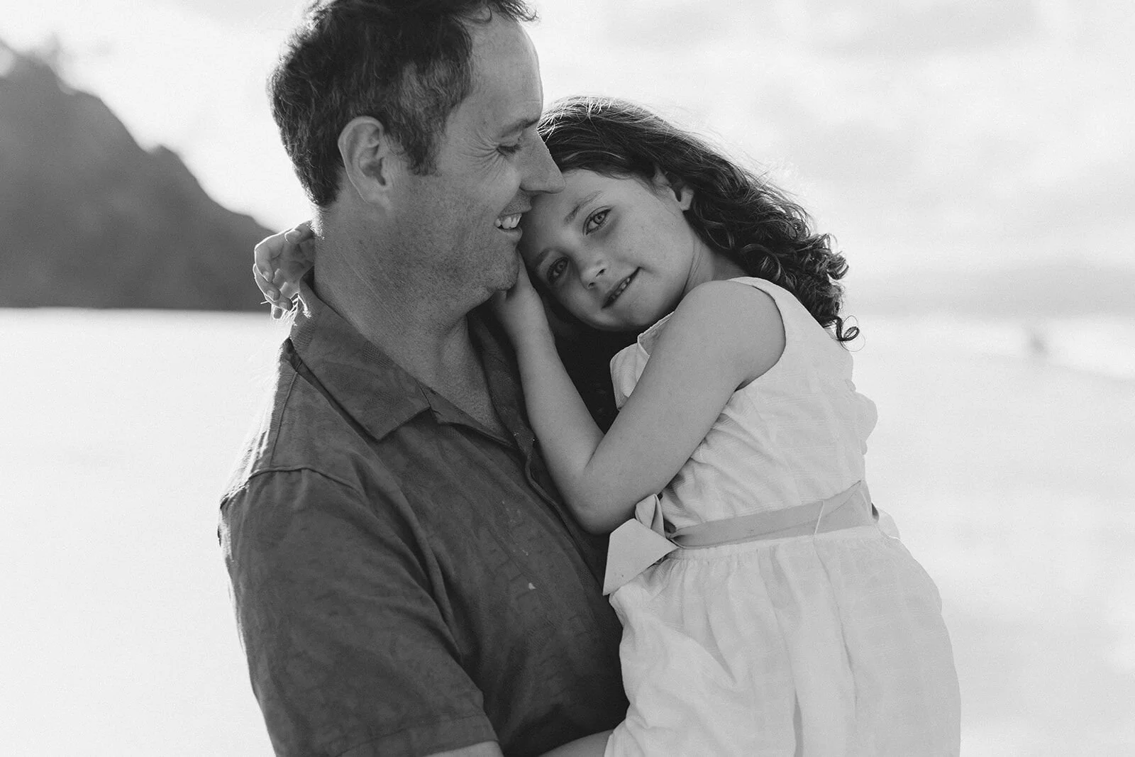 Black and white photo of a dad hugging his daughter close on the beach