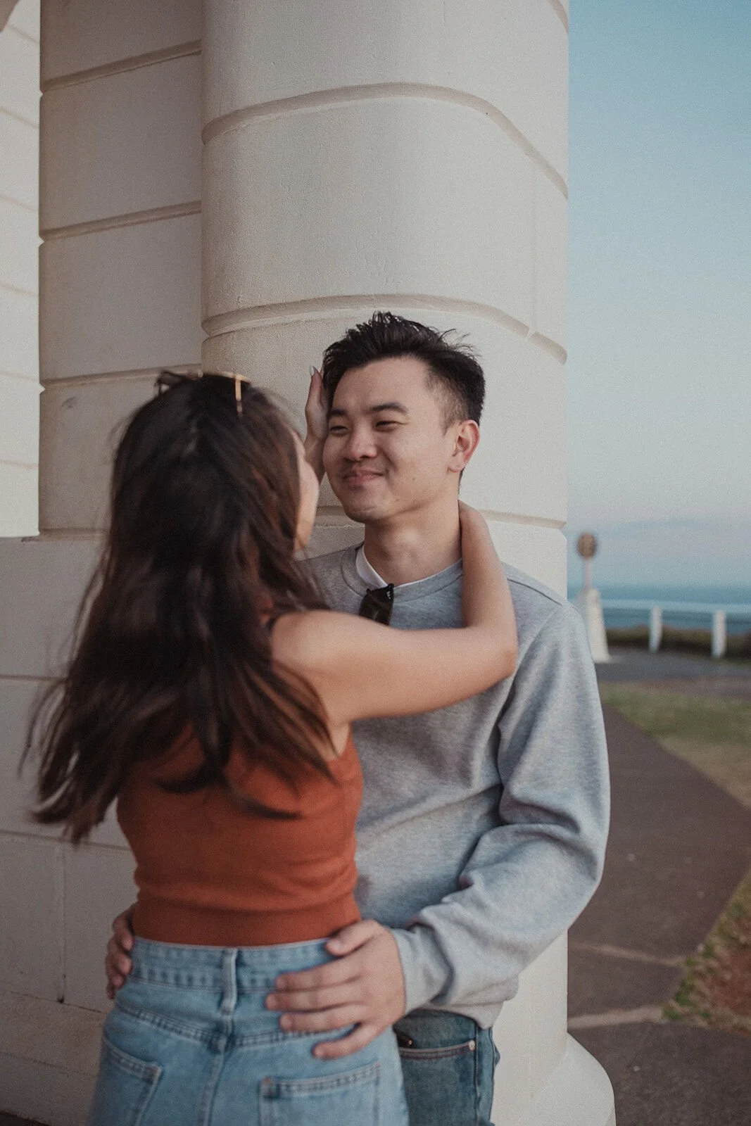 Woman reaching up to touch her fiancé's face beside the lighthouse, Douglas and Ying's sunset marriage proposal at Cape Byron Lighthouse, Byron Bay