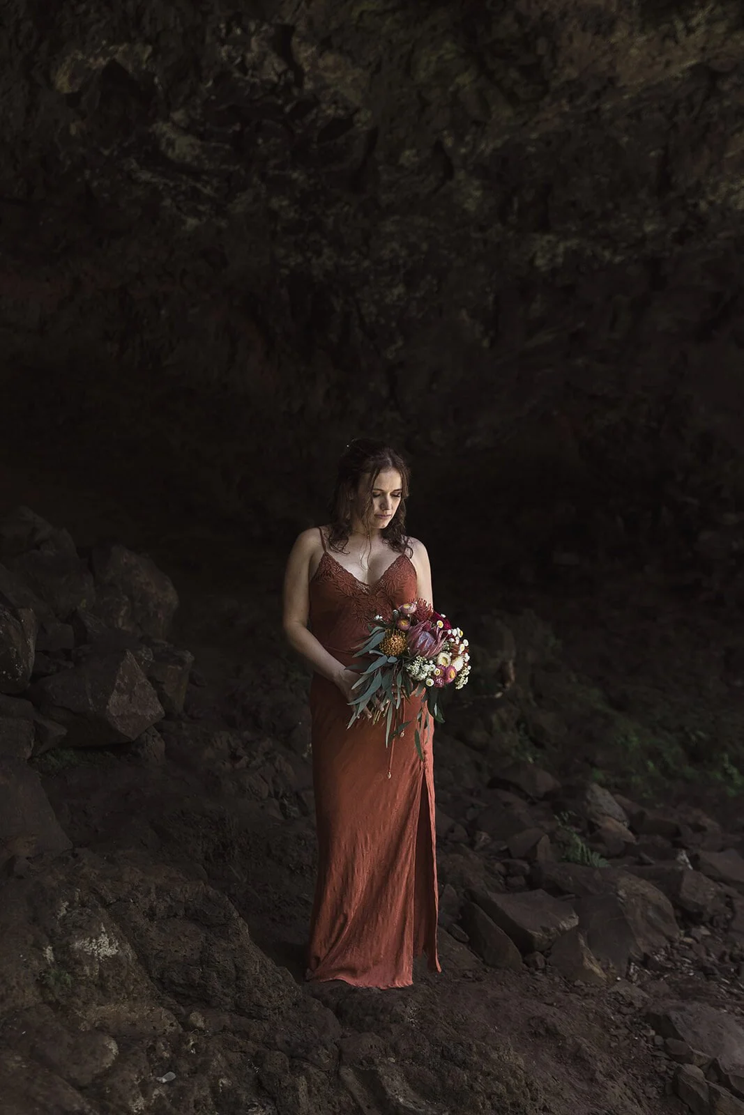 Bride looking down at her bouquet in the cave, Sara and Graeme's elopement at Killen Falls, Northern Rivers