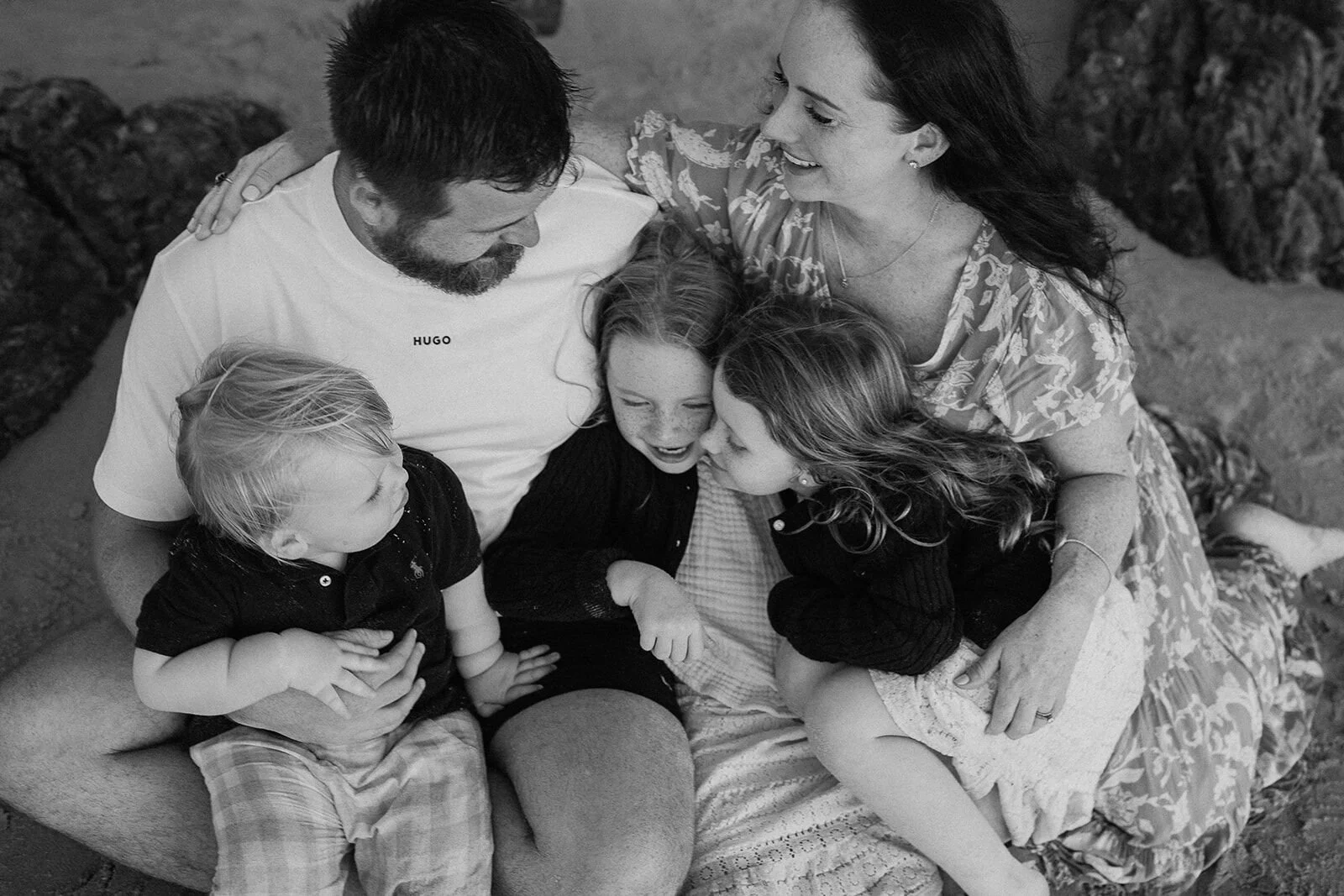 Black and white photo of a family cuddled close together on the rocks, laughing