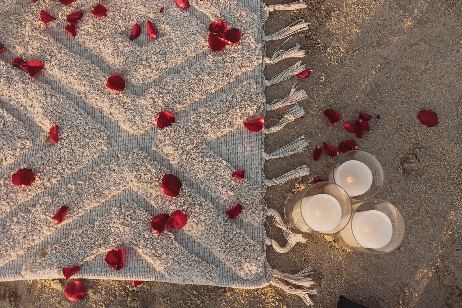 Detail of a woven rug scattered with red rose petals and candles, Charlie and Hannah's sunrise marriage proposal at Broken Head Beach, Byron Bay