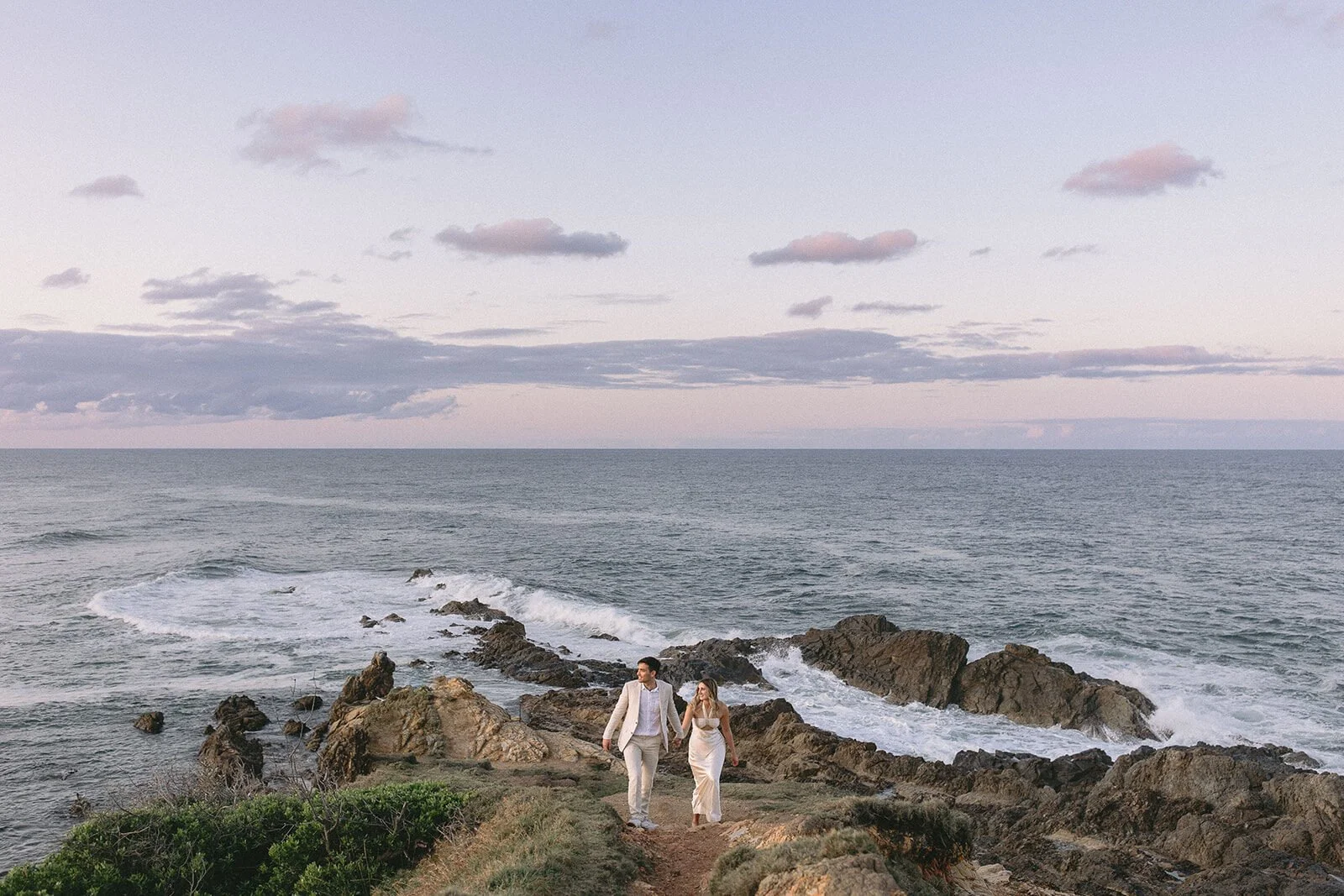 Couple walking along the clifftop track above the sea, Abby and James' elopement at Little Wategos Beach, Byron Bay