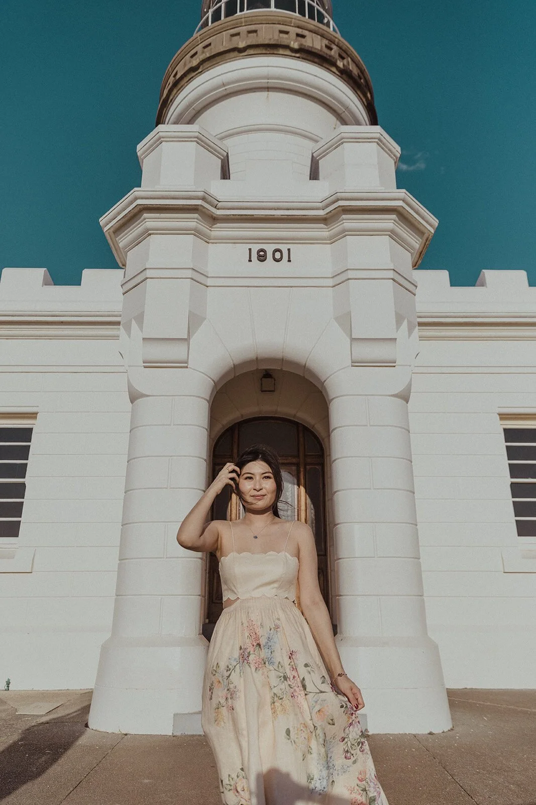 Bride in a floral dress at the lighthouse entrance, Maggie and William's pre-wedding photos in Byron Bay